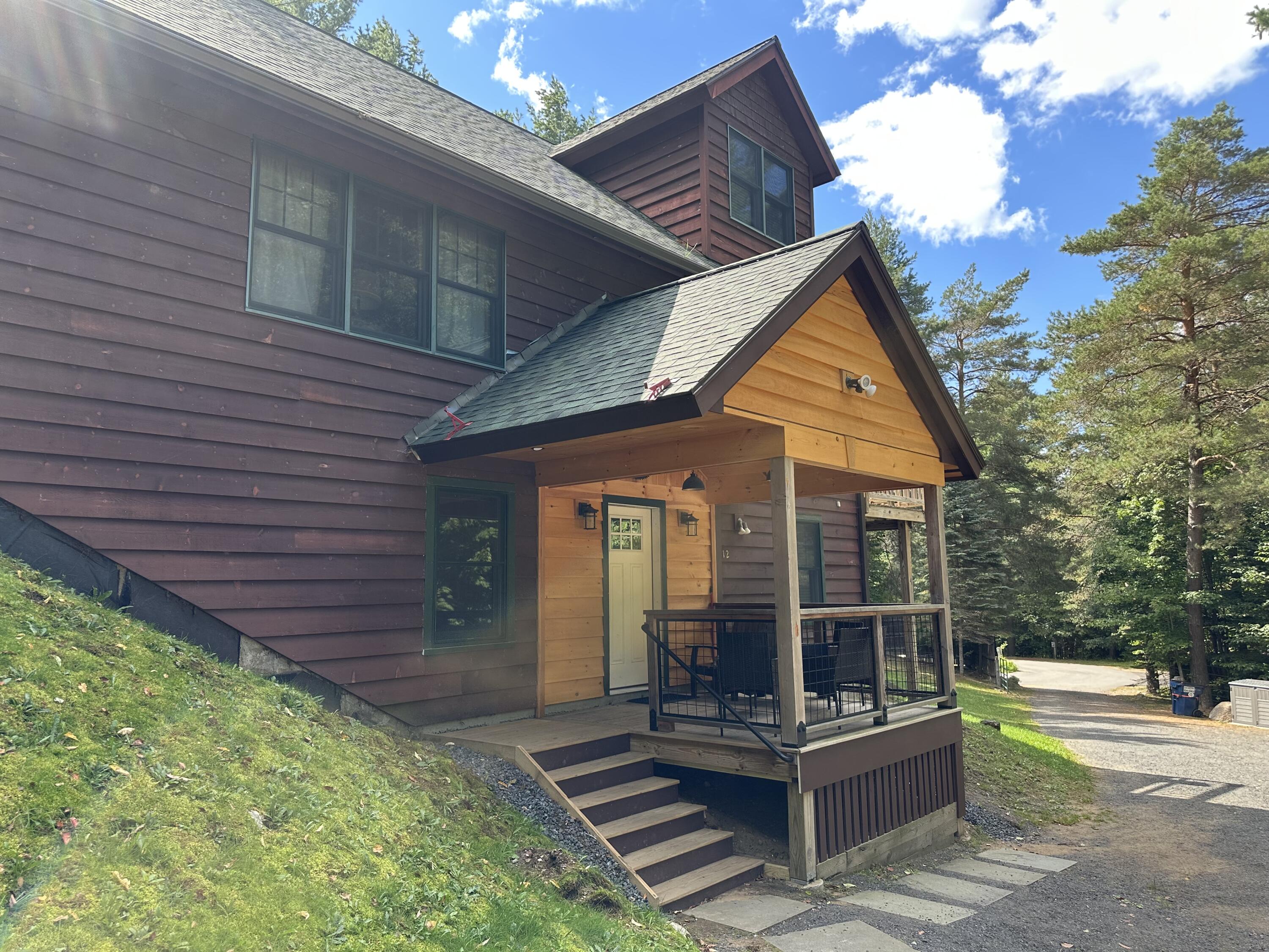 Two-story brown house with a timber-accented covered porch and front steps among tall trees.