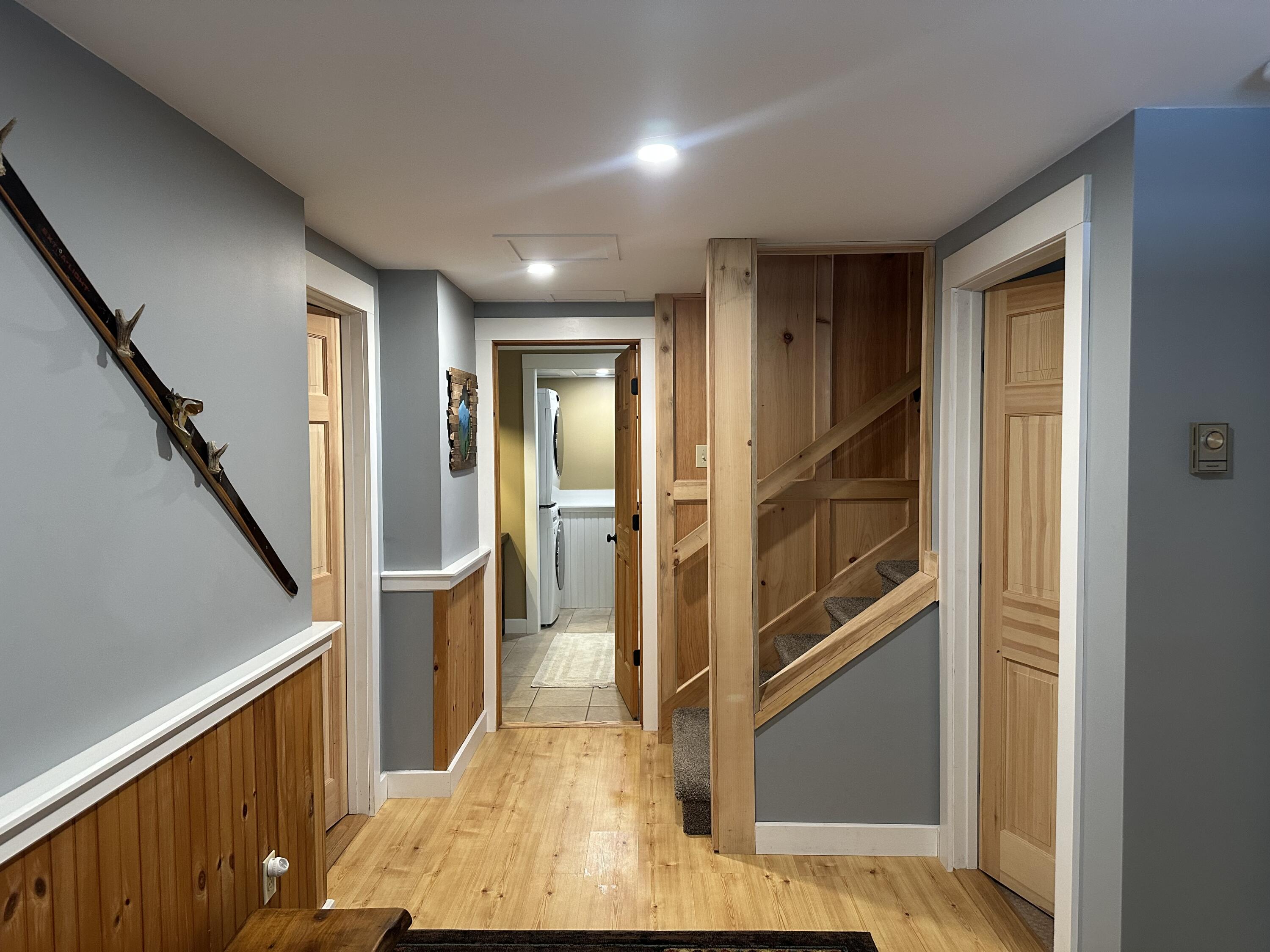 Hallway with wood flooring and wainscoting, gray walls, and a carpeted staircase.