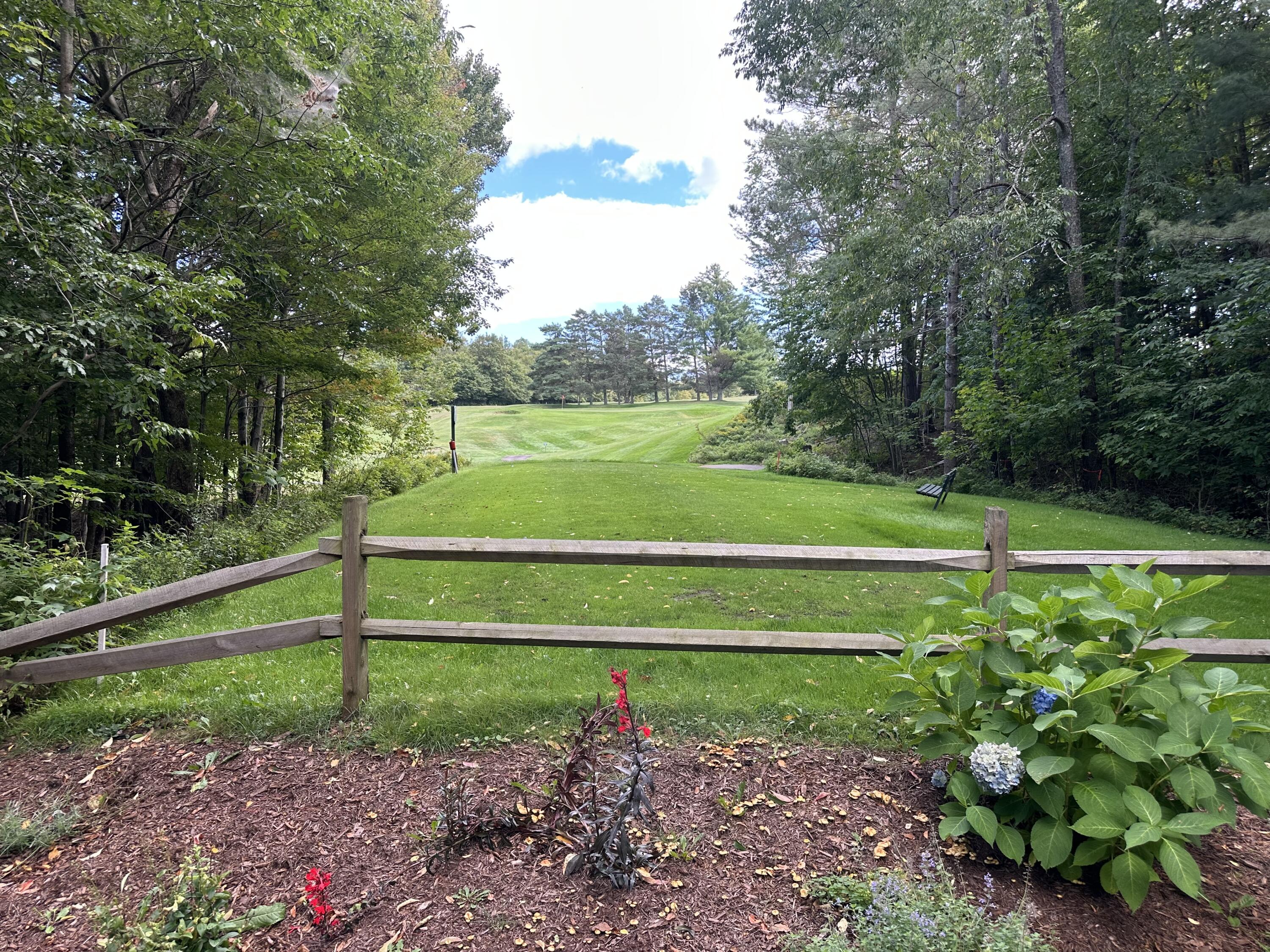 Landscaped lawn and wooden fence overlooking a tree-lined golf course.