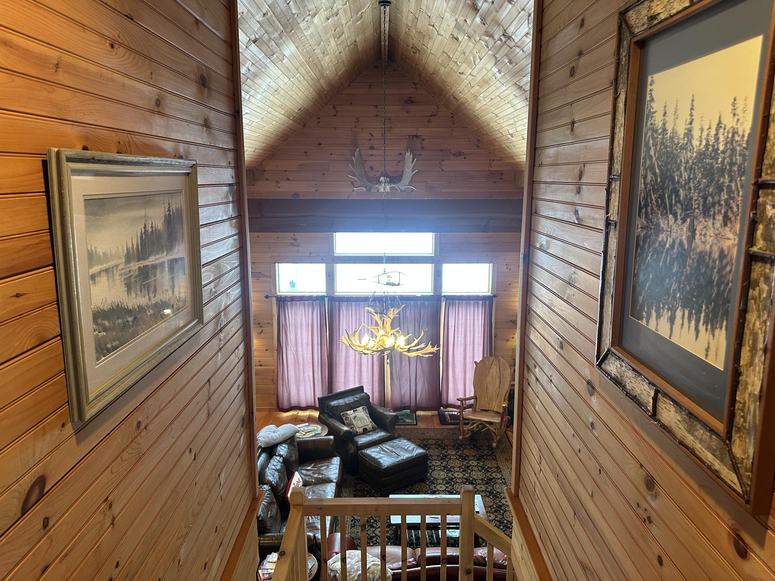 Wood-paneled staircase overlooks a vaulted living room with leather seating and an antler chandelier.