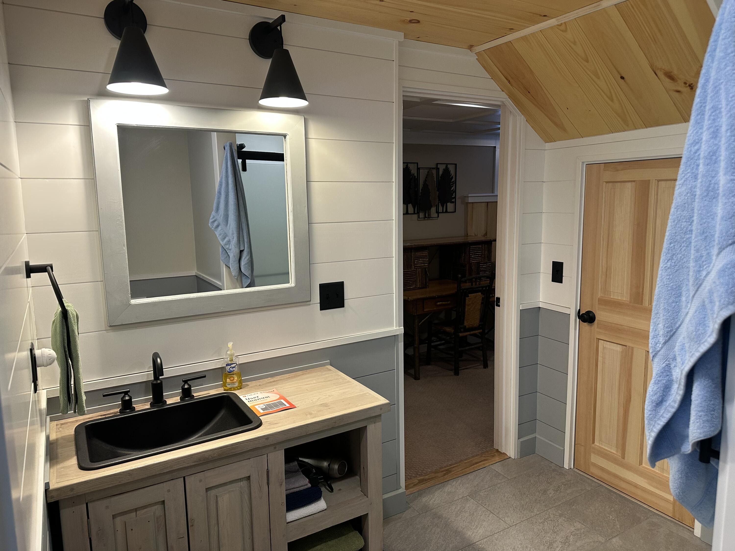 Bathroom with black vessel sink, wood vanity, paneled walls, and a sloped wood ceiling.