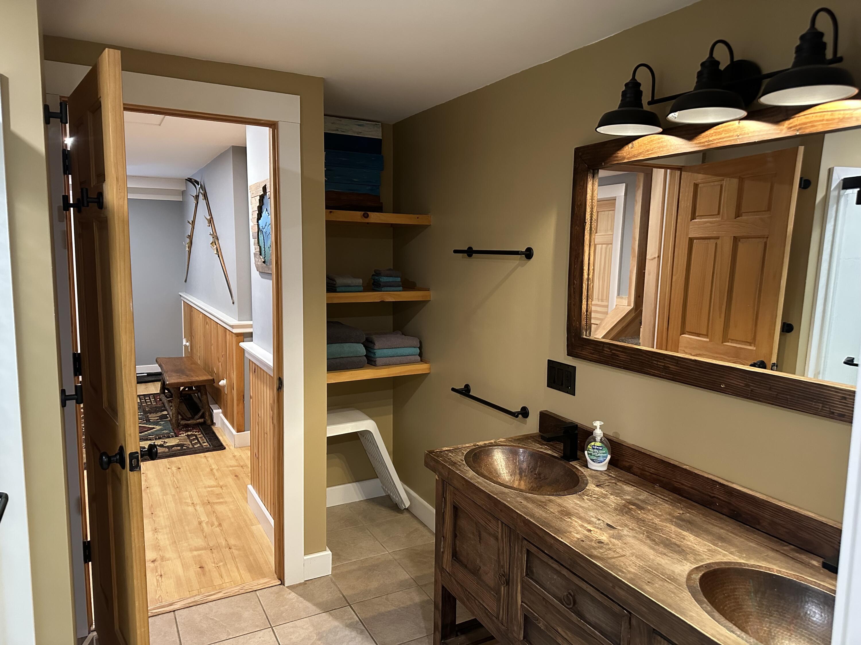 Bathroom with a rustic wooden double vanity, two copper sinks, and open towel shelves.