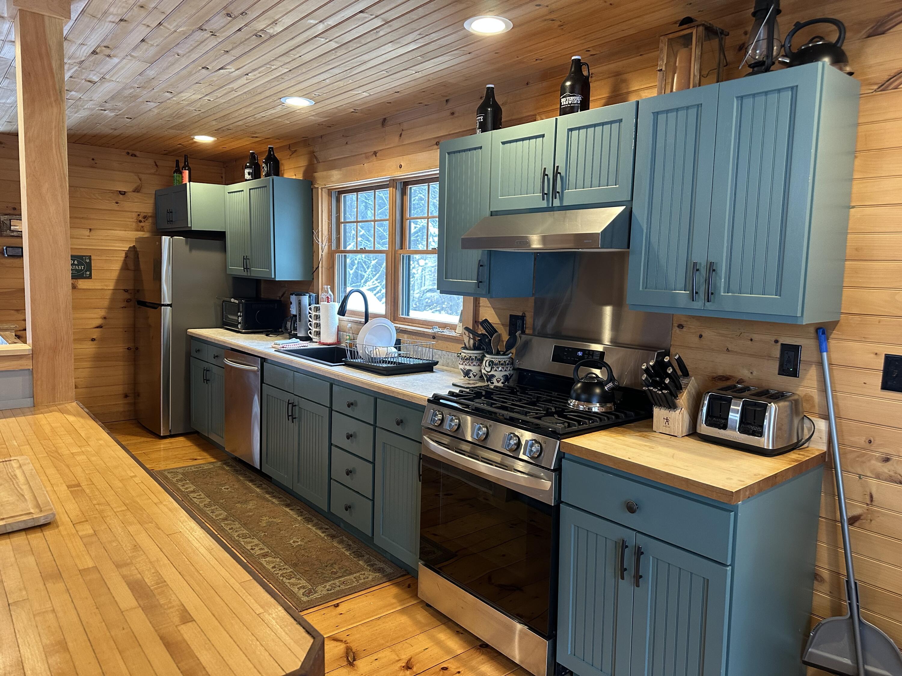 Cabin kitchen with blue-green cabinets, butcher-block counters, and a stainless gas range.
