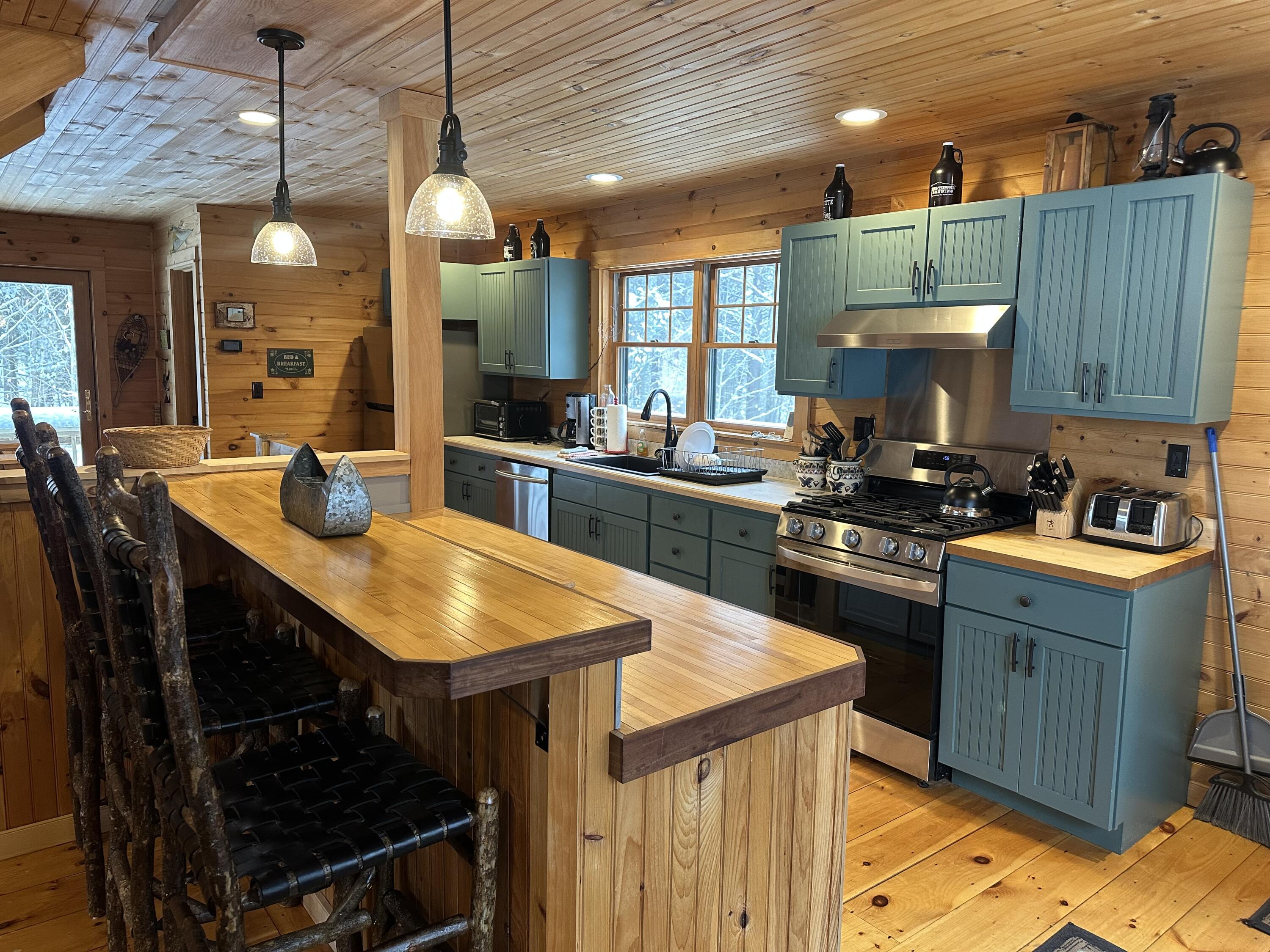 Log-cabin kitchen with blue-green cabinets, stainless appliances, and a large wooden island.