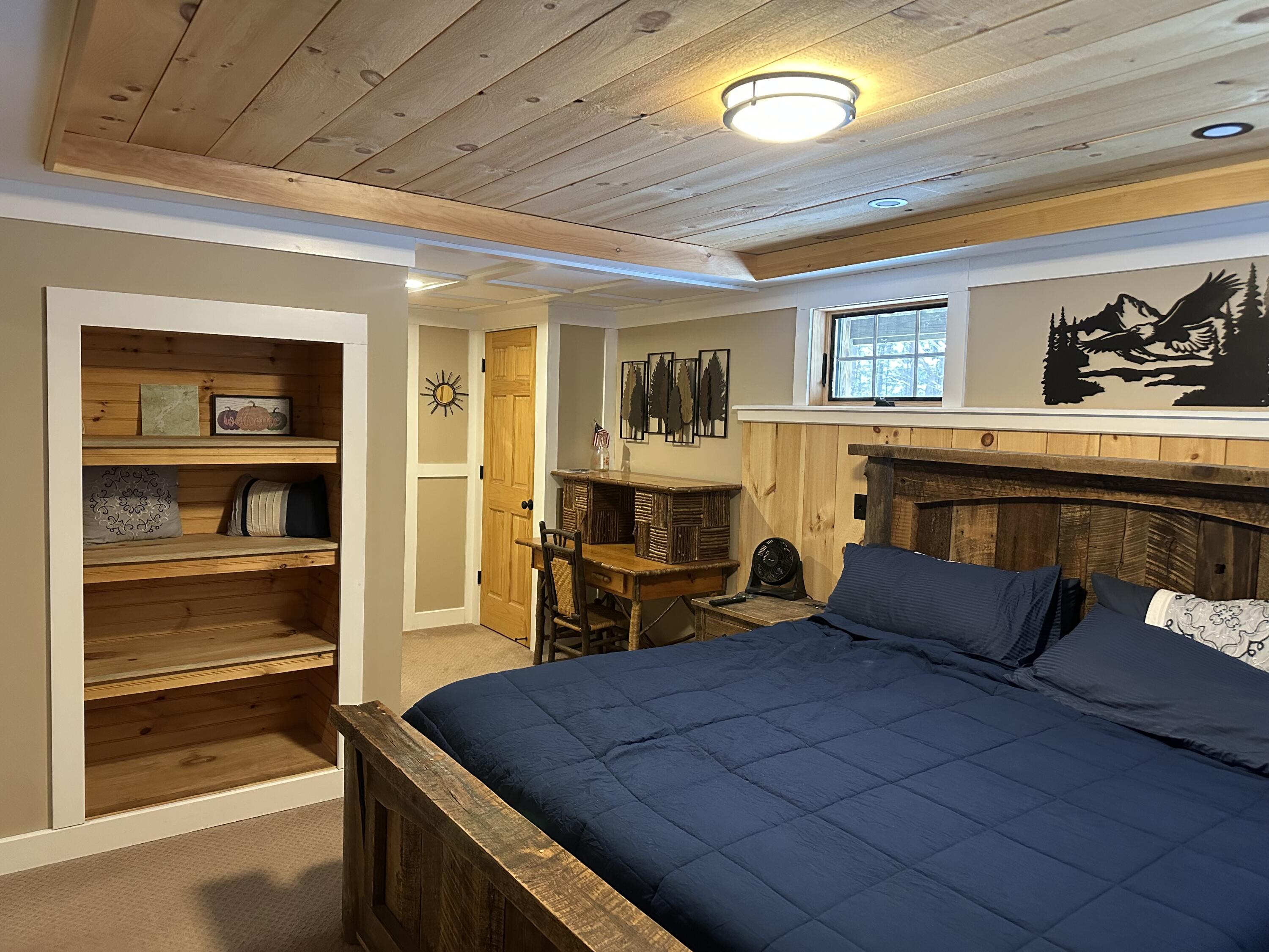 Bedroom with a rustic wooden bed, navy bedding, built-in shelves, and a wood plank ceiling.