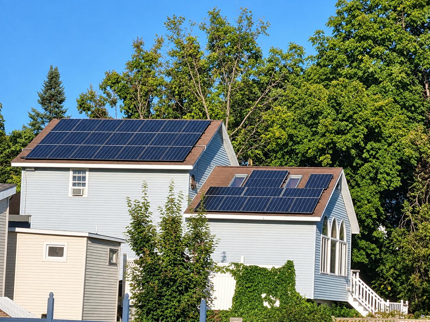 Light blue house with solar panels on both roofs and tall arched windows.