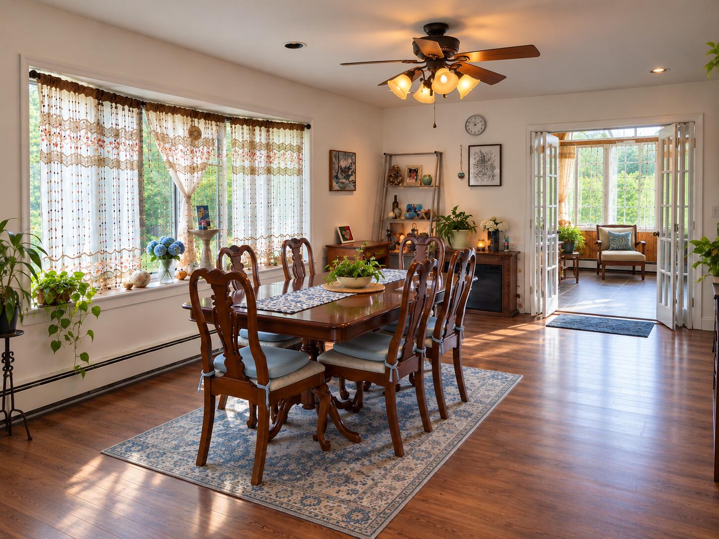 Dining room with a long wooden table, patterned rug, and open doors to a bright sunroom.