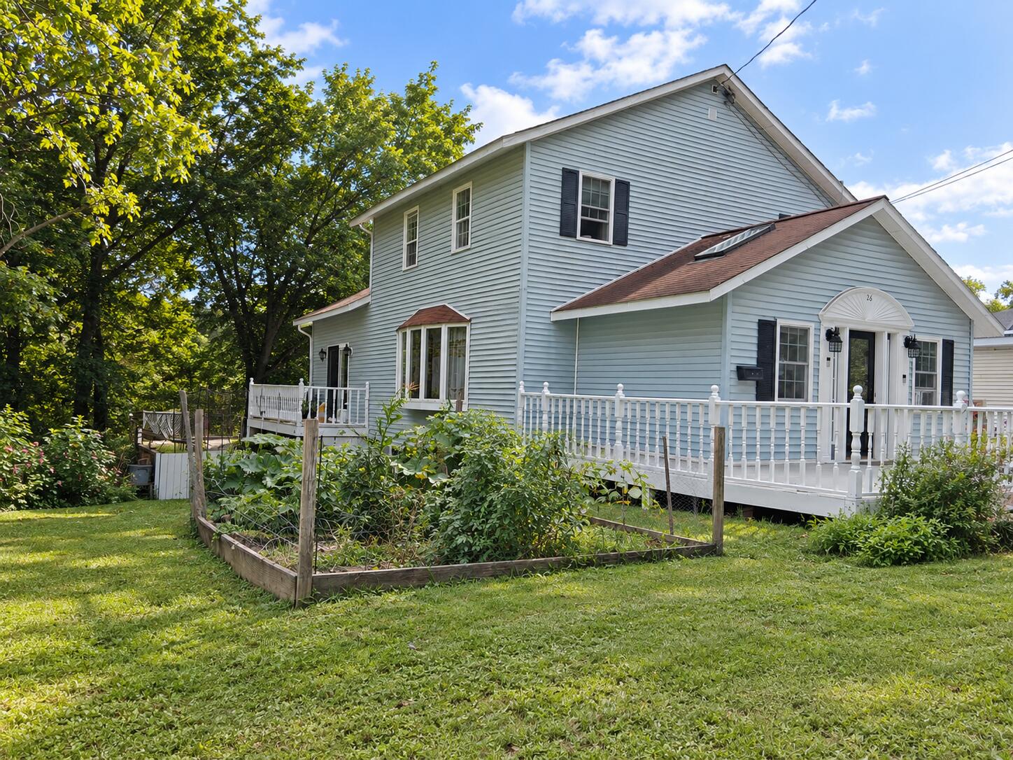 Light blue two-story house with a white porch beside a fenced vegetable garden.