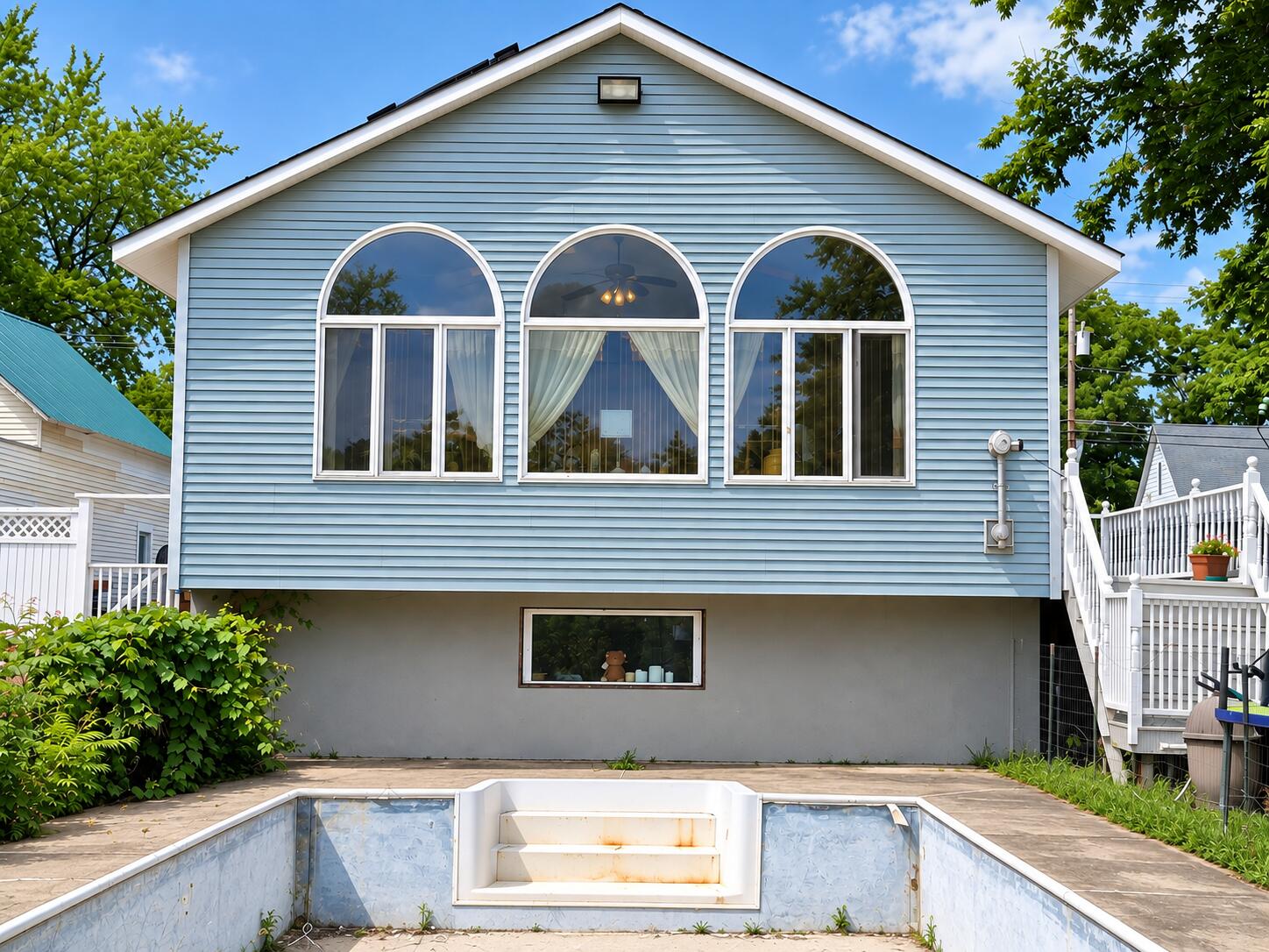 Light blue house with three arched windows behind an empty in-ground pool.