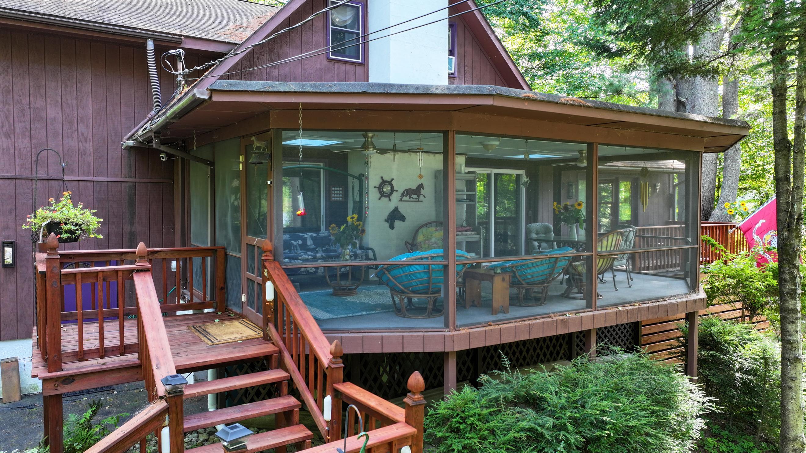 Screened porch with seating and wooden deck stairs surrounded by trees.
