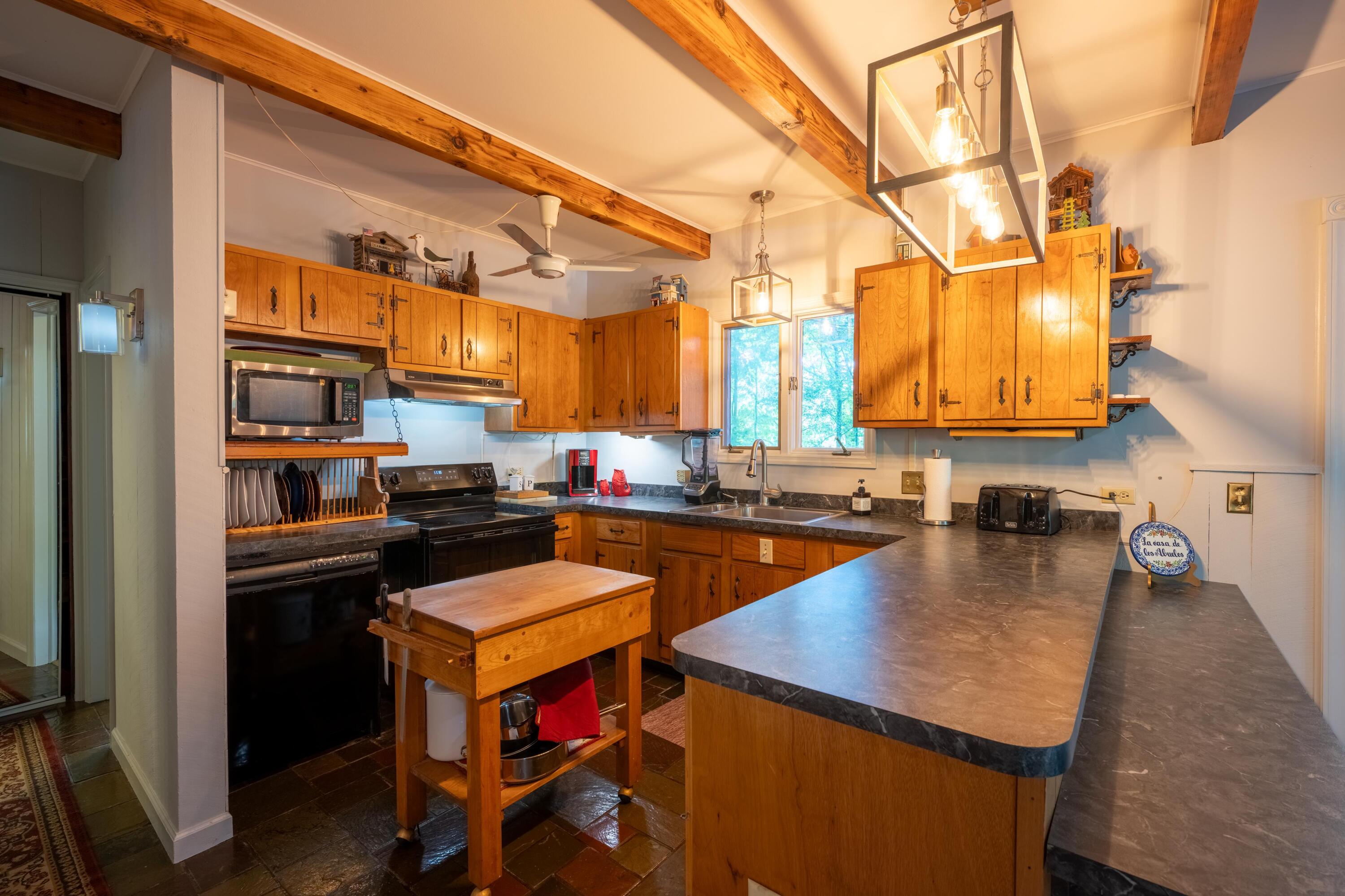 Rustic kitchen with honey-colored wood cabinets, exposed beams, and a large dark countertop peninsula.