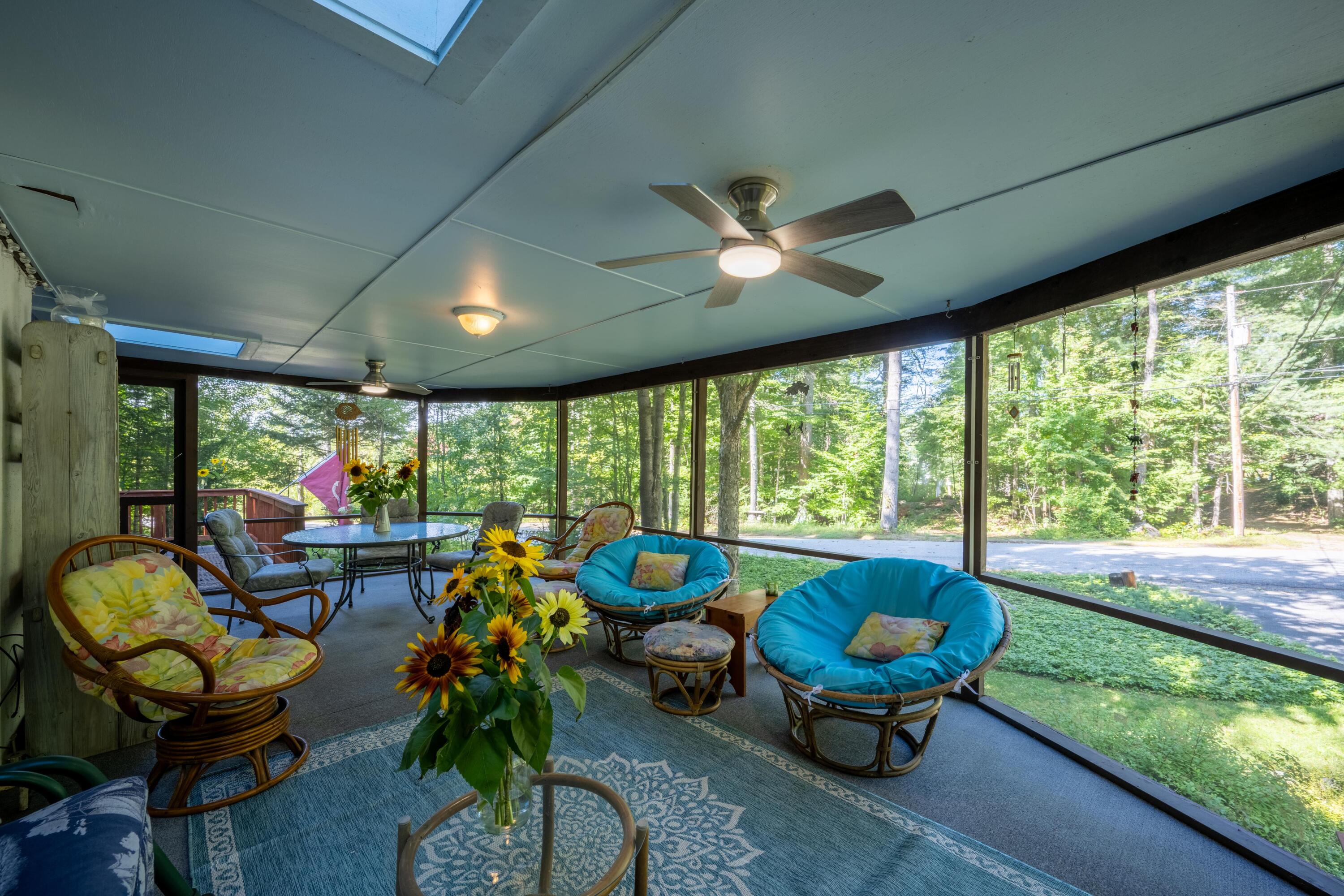 Screened porch with wicker seating and blue cushions overlooking leafy woods.