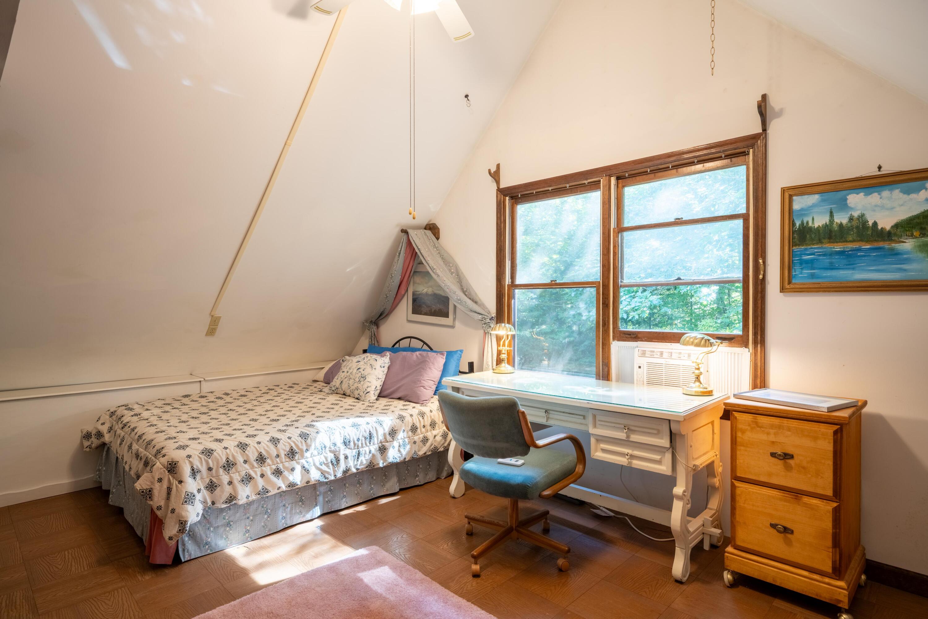 Bedroom with a sloped ceiling, canopy bed, and desk beside large wood-trimmed windows.