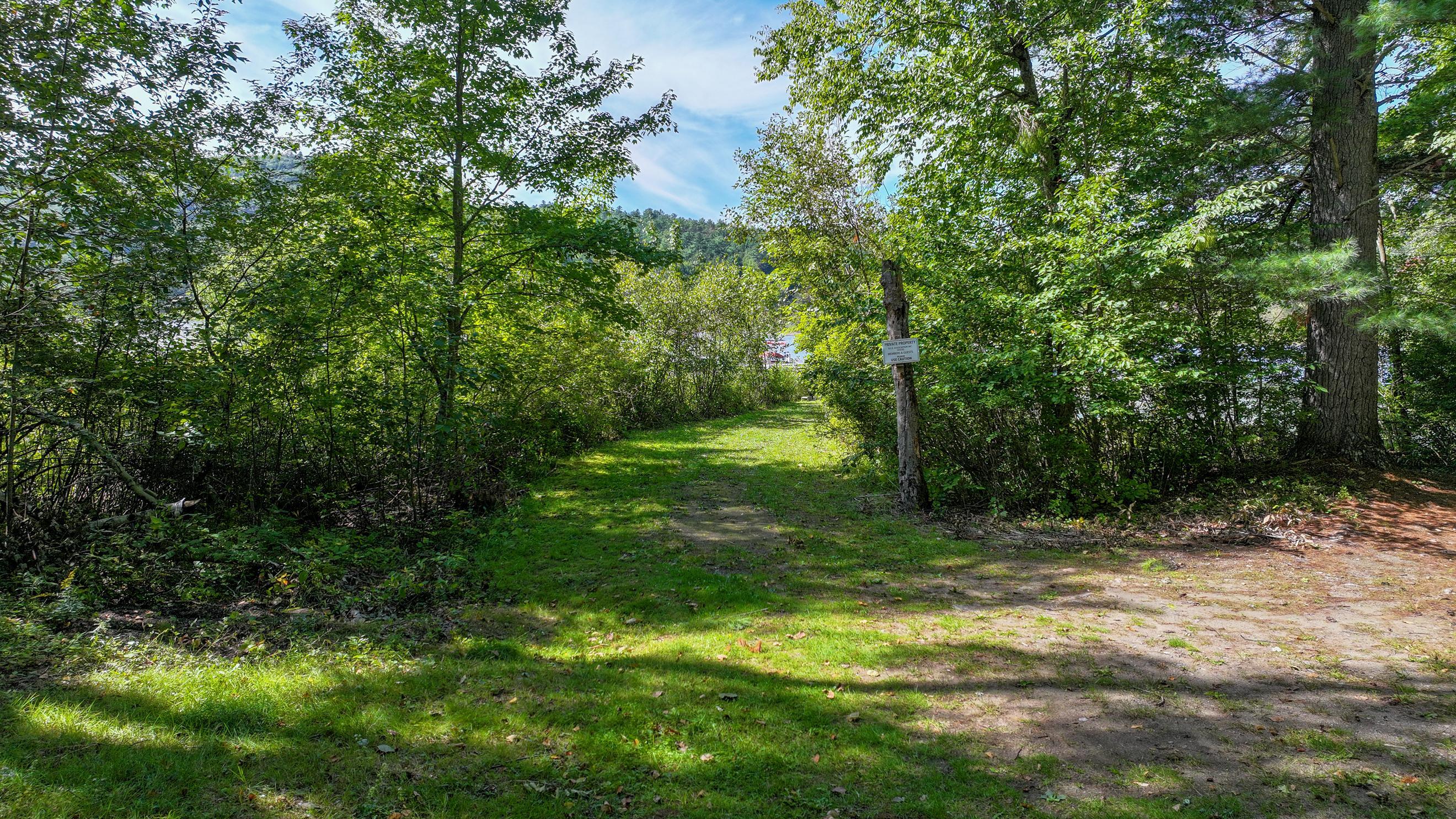 Wooded property entrance with a grassy path, private property sign, and dirt drive.