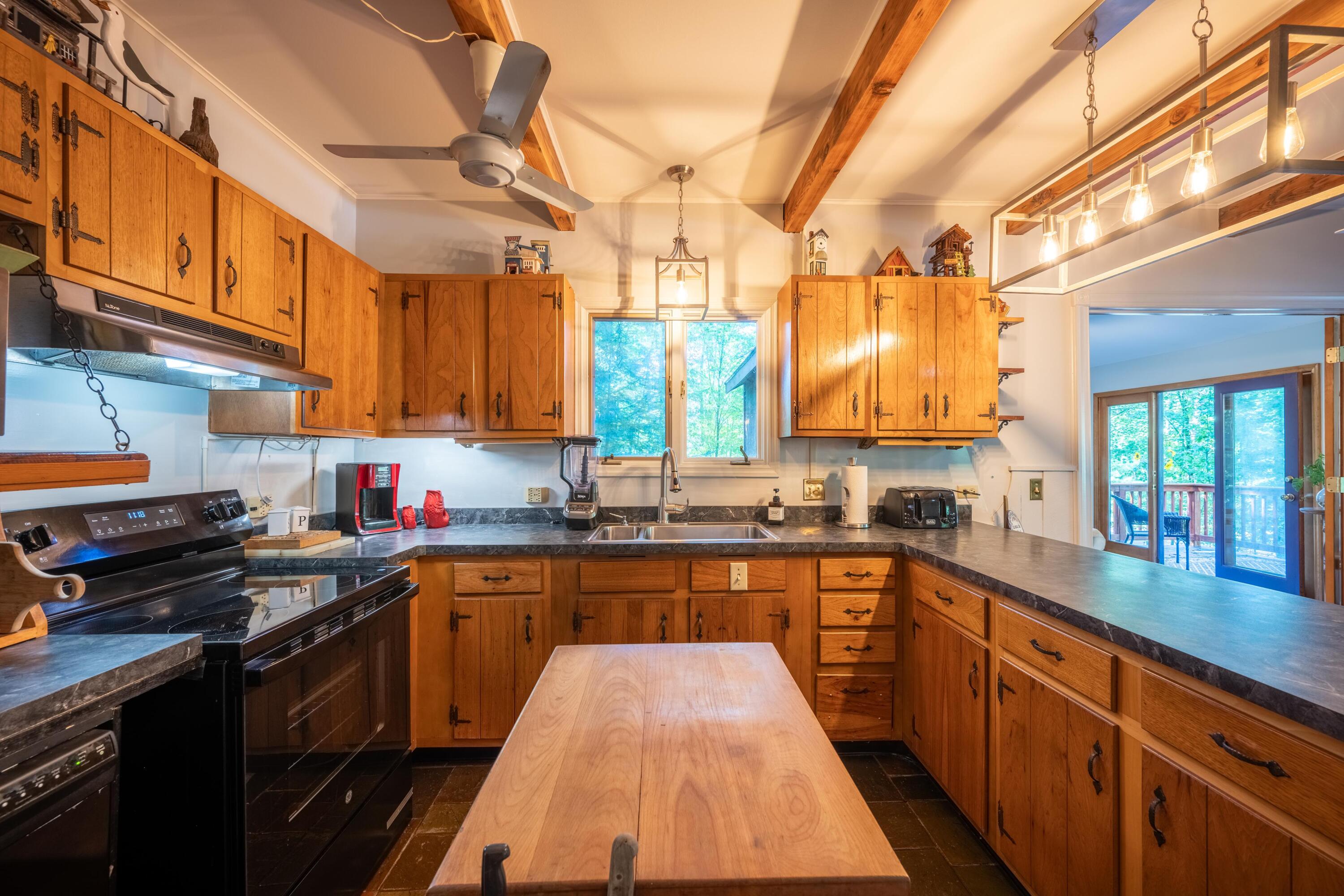 Rustic kitchen with honey-colored cabinets, dark countertops, and a central butcher-block island.