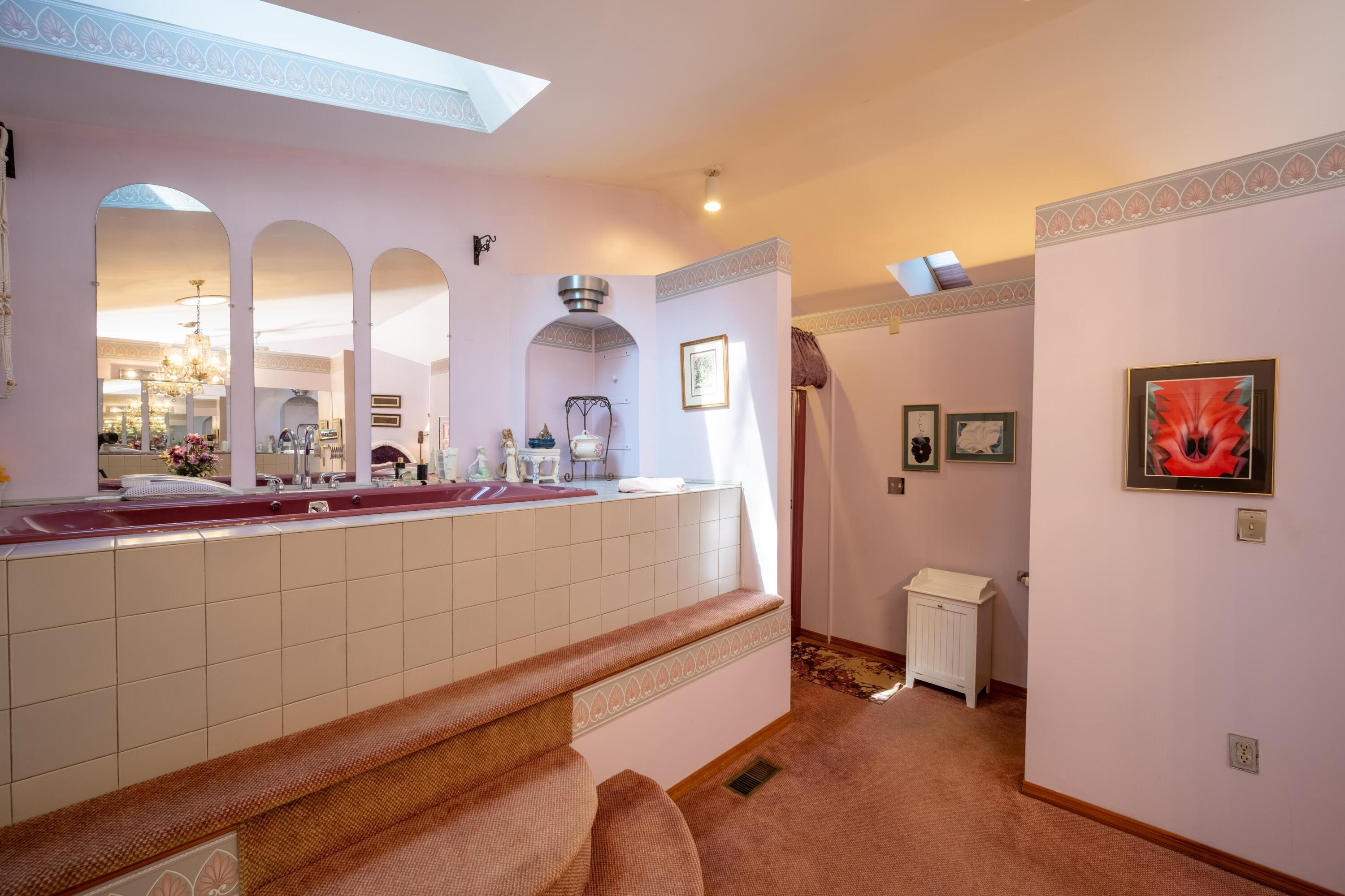 Bathroom with a large raised jetted tub, arched mirrors, and skylights.