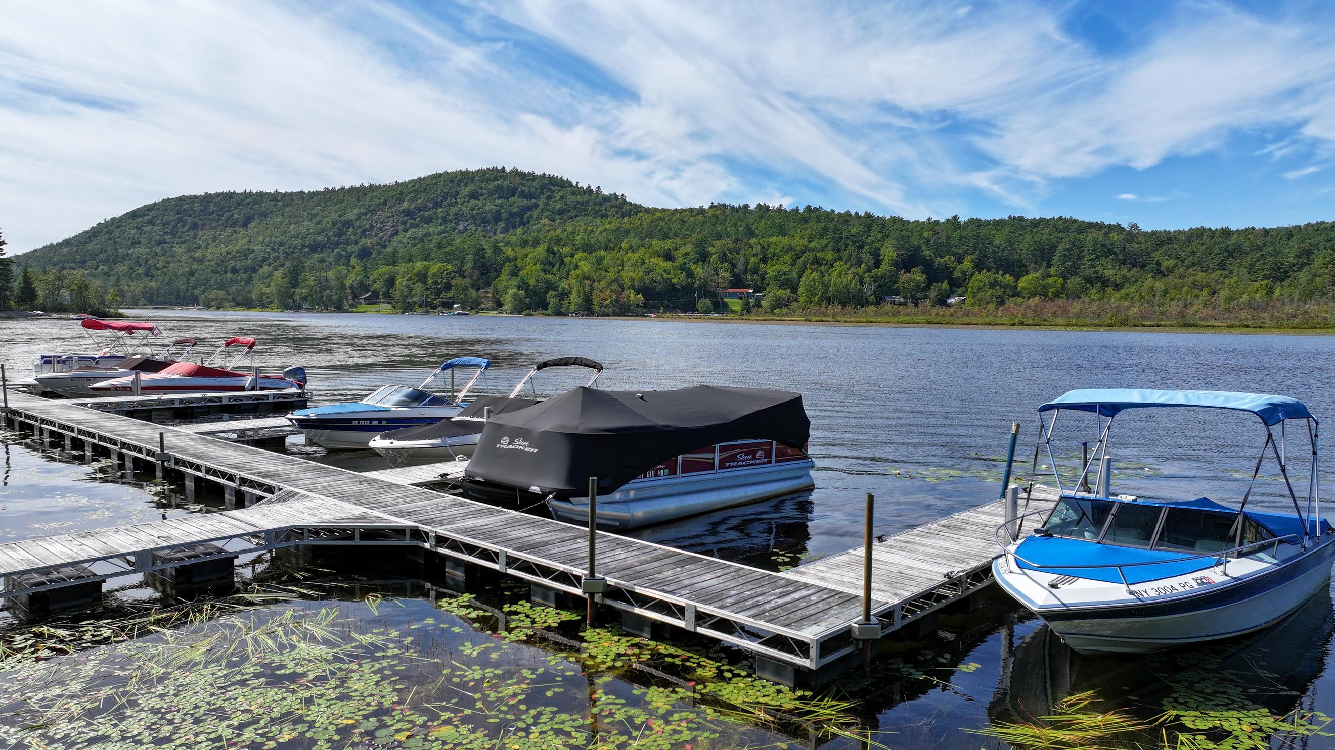 Lakeside dock with moored boats, lily pads, and wooded hills across the water.