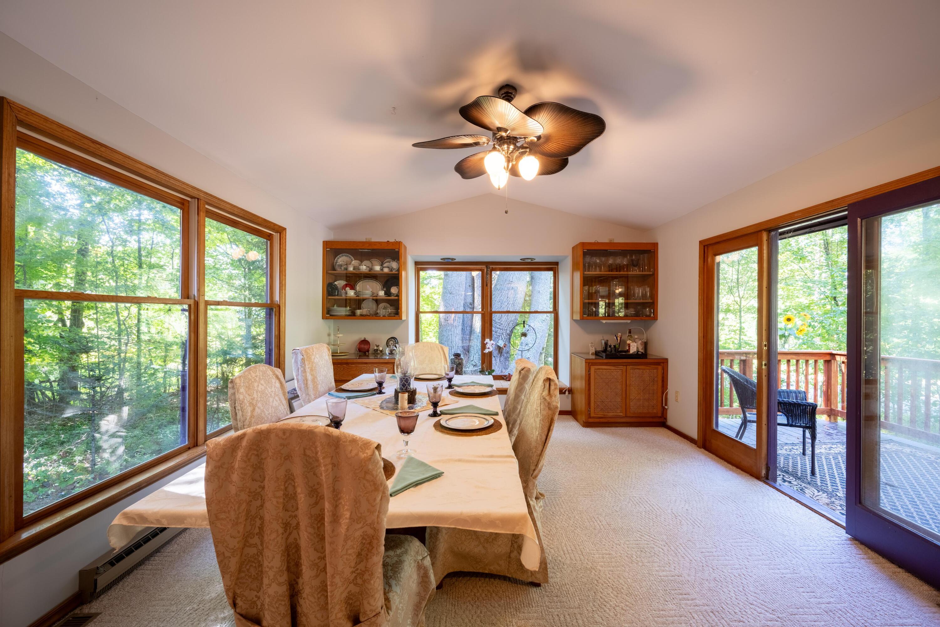 Dining room with a set table, large wooded-view windows, and sliding doors to a deck.