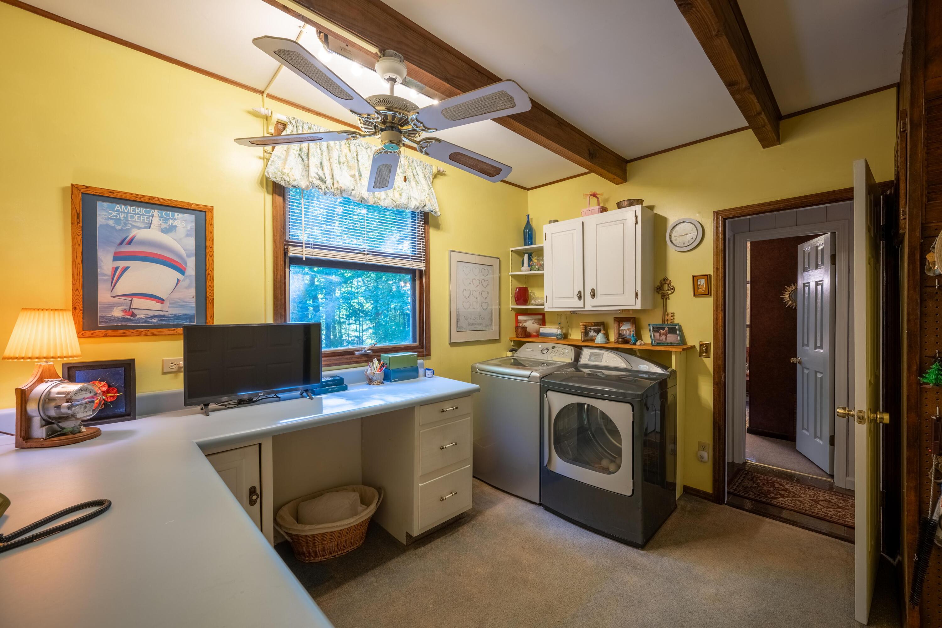Laundry room with washer and dryer, white cabinets, and a long countertop beneath a window.