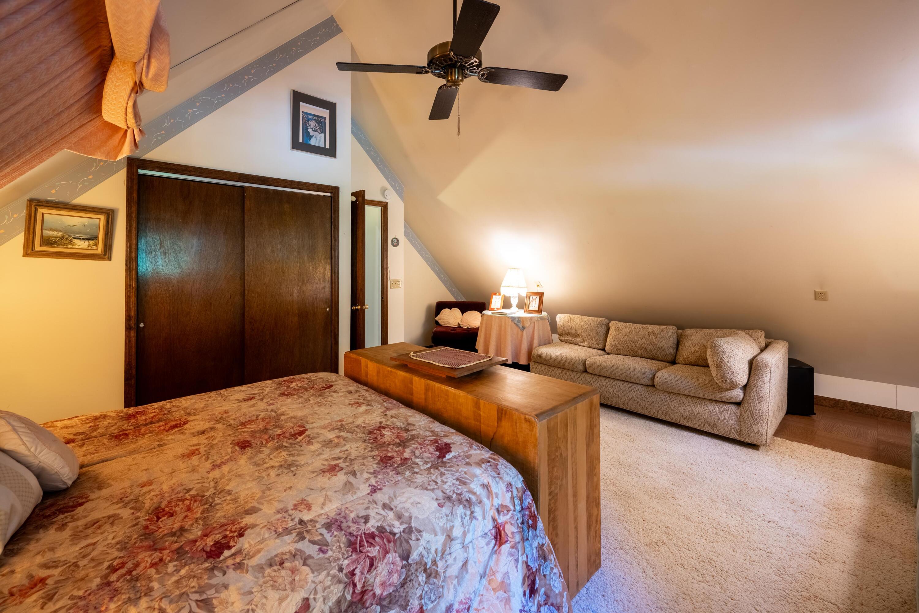 Bedroom with floral bedspread and a sitting area beneath a sloped ceiling.