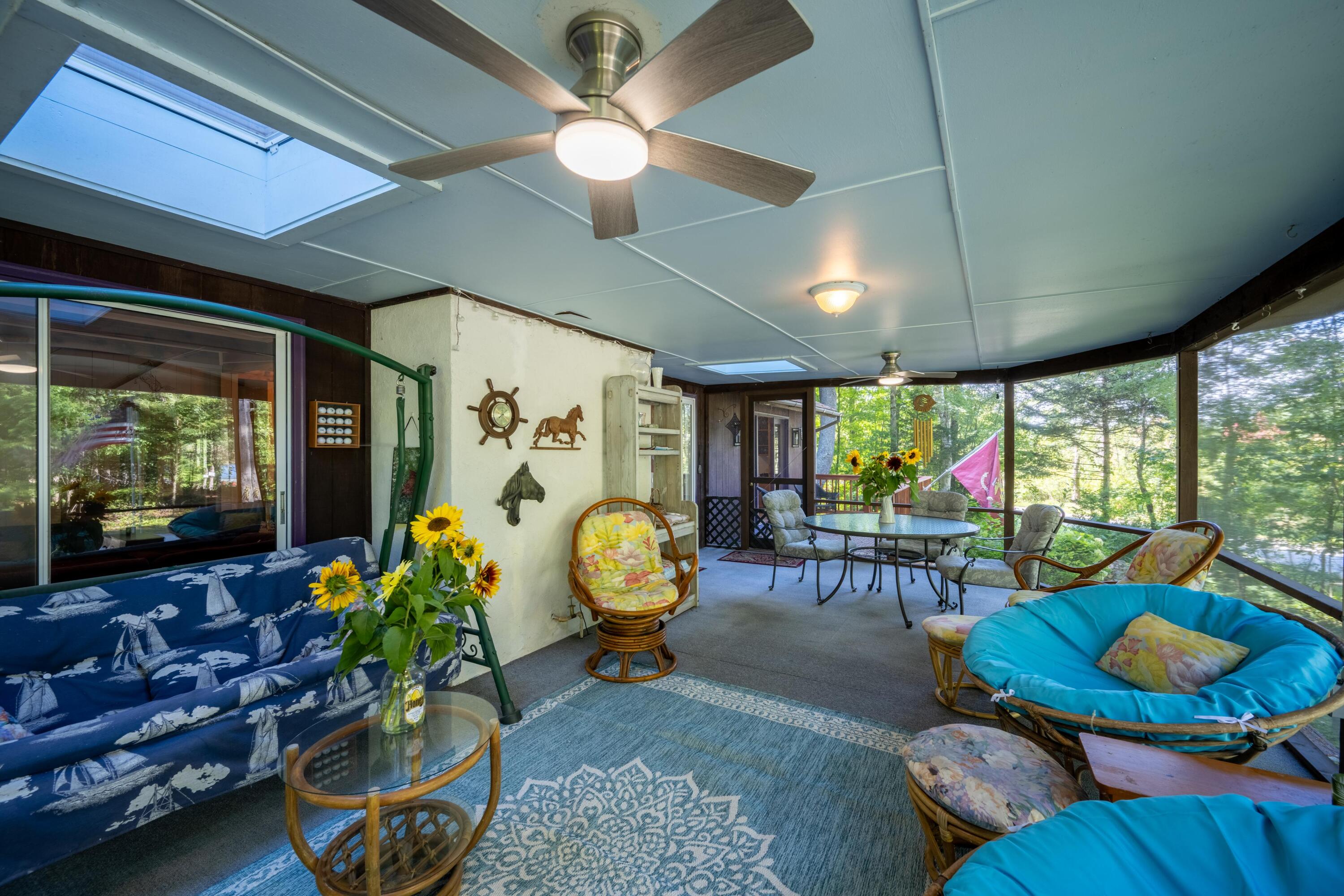 Furnished enclosed porch with skylights, ceiling fans, colorful seating, and wooded water views.