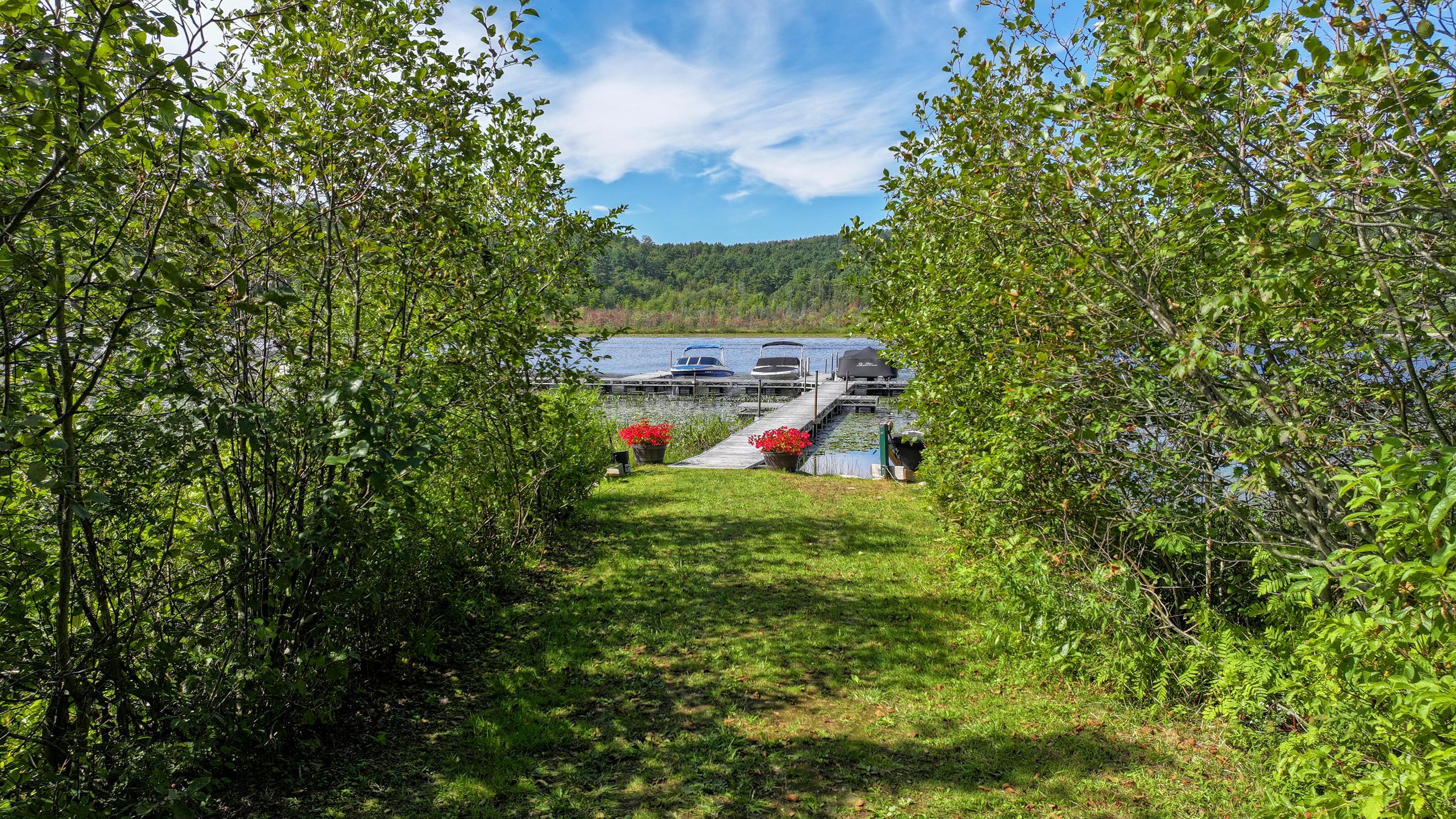 Lakefront dock with boats, approached across a grassy lawn through leafy trees.
