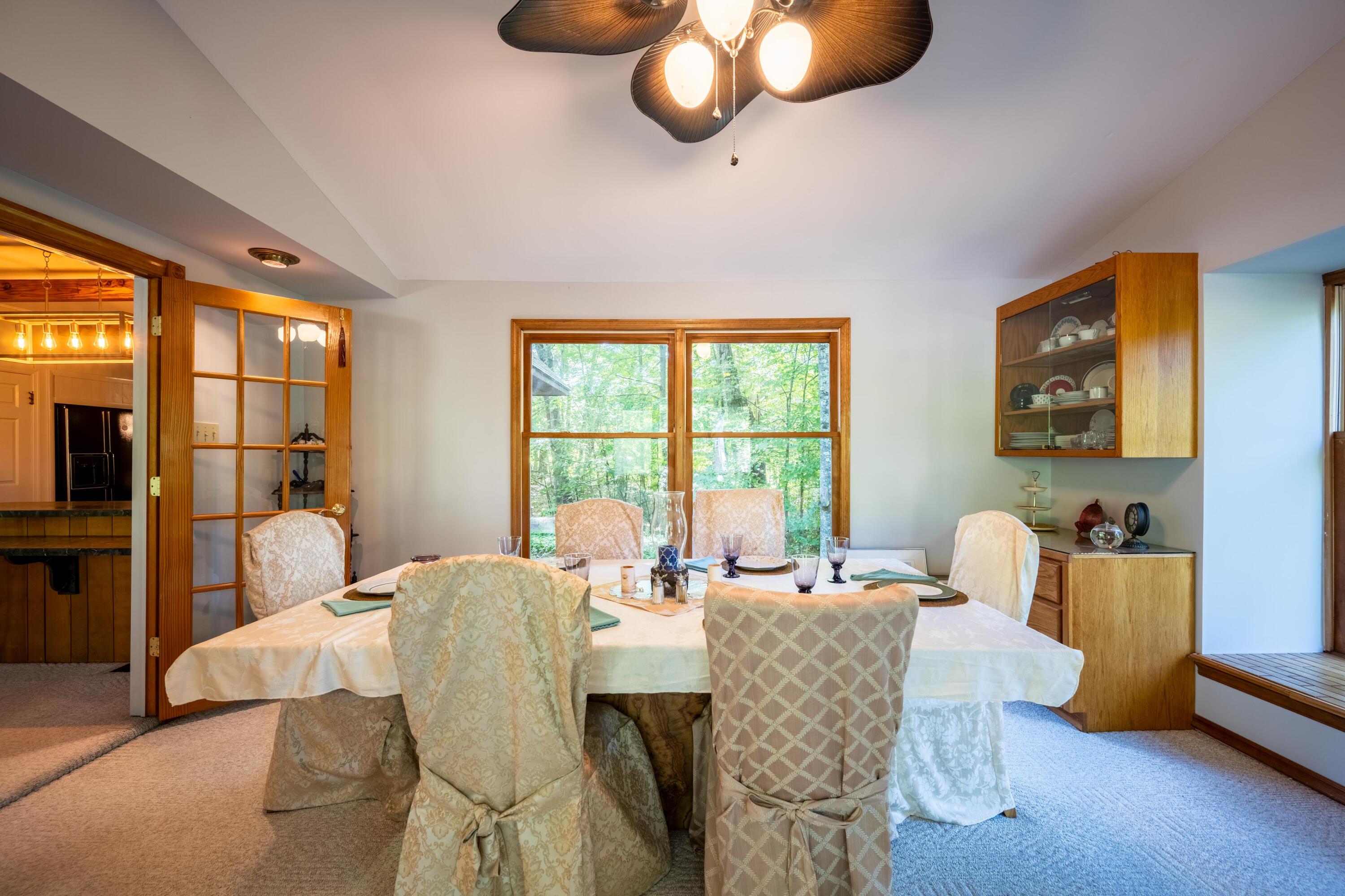 Furnished dining room with a set table, wood-trimmed windows, and a glass-front china cabinet.