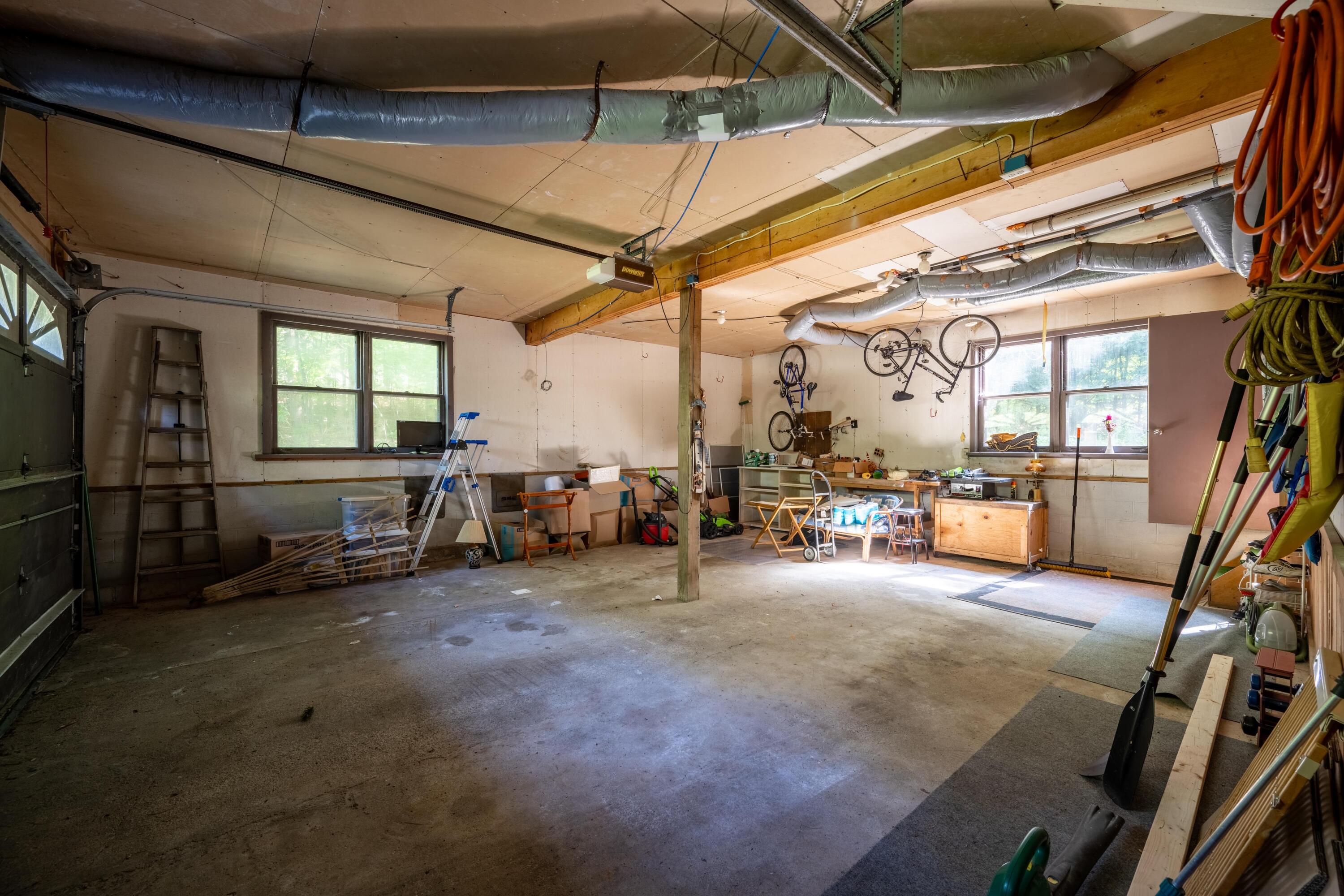 Spacious garage workshop with hanging bicycles, tools, exposed ducts, and a broad concrete floor.