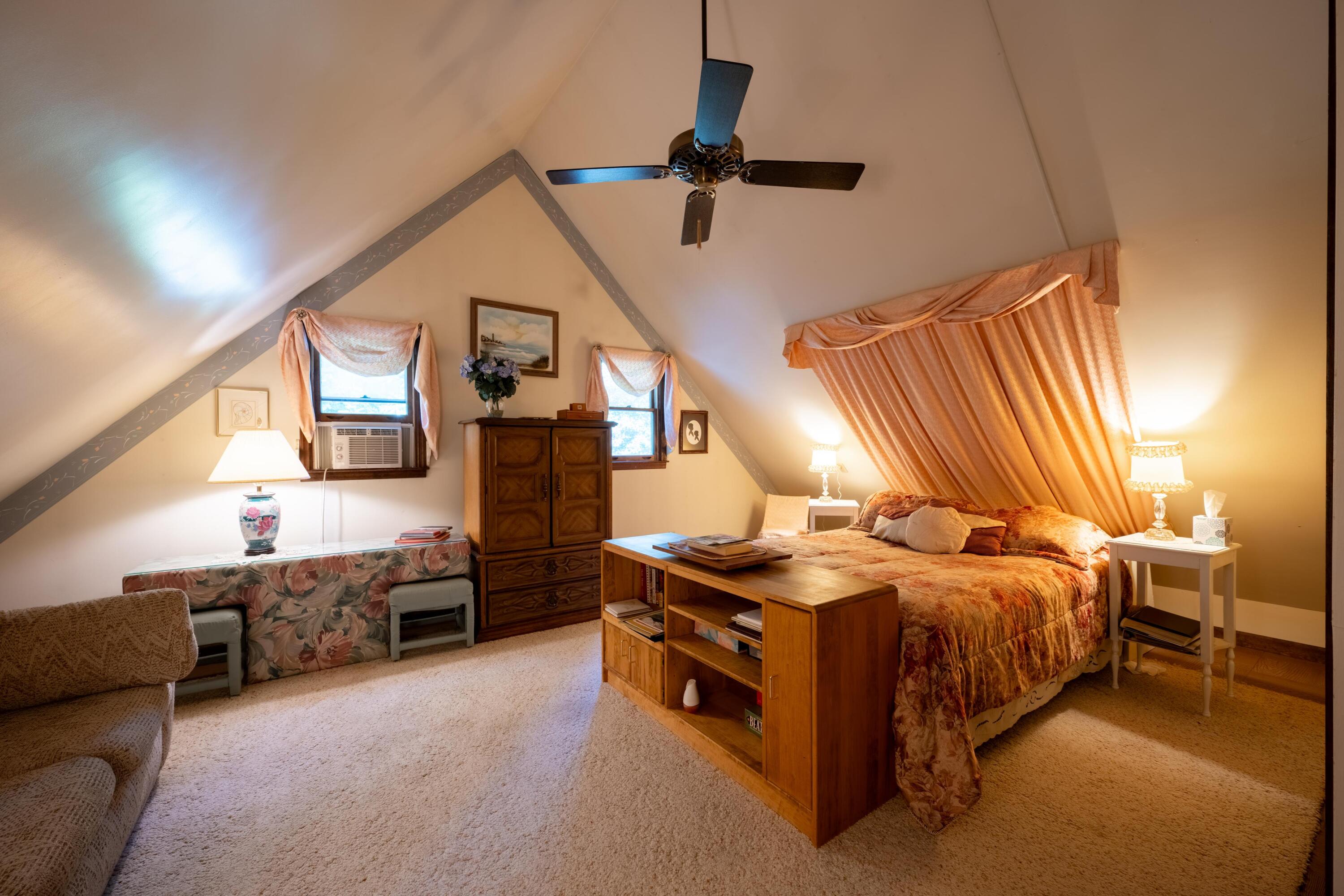 Attic bedroom with a sloped ceiling, peach curtains, a large bed, and a wooden bookcase.