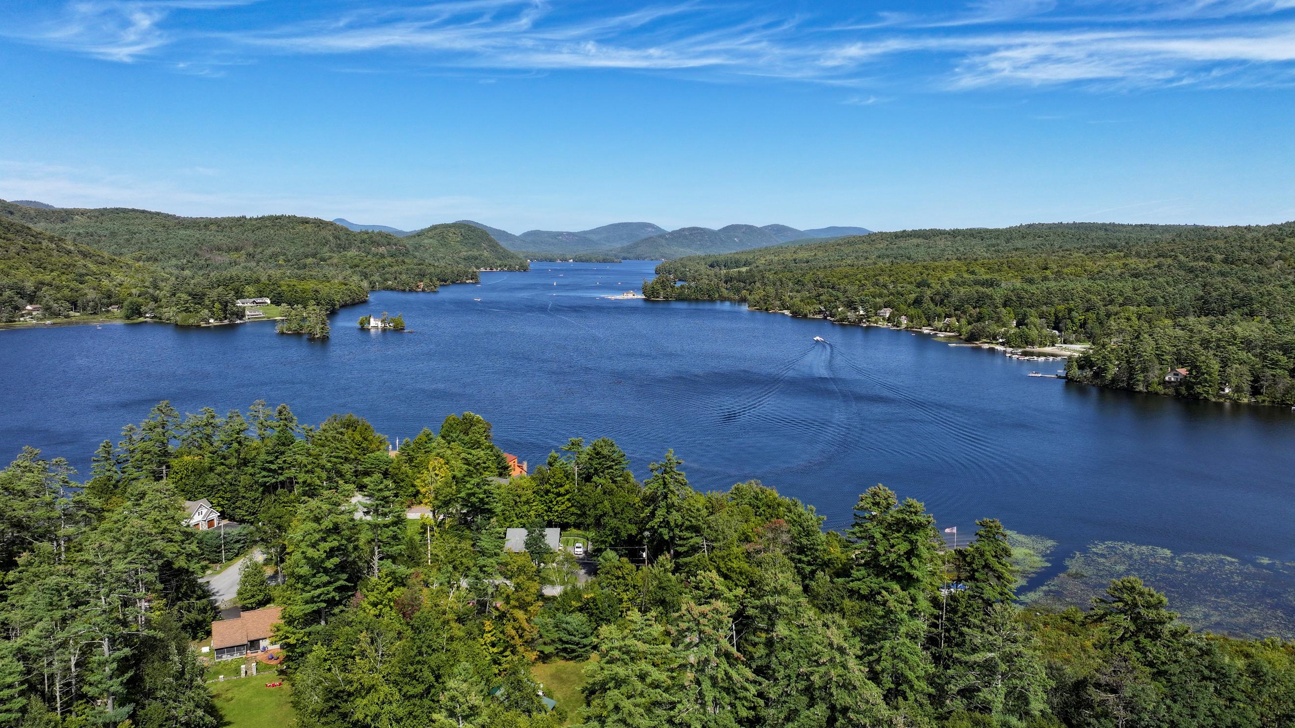 Aerial view of Brant Lake, with forested shores, distant hills, and a boat wake.