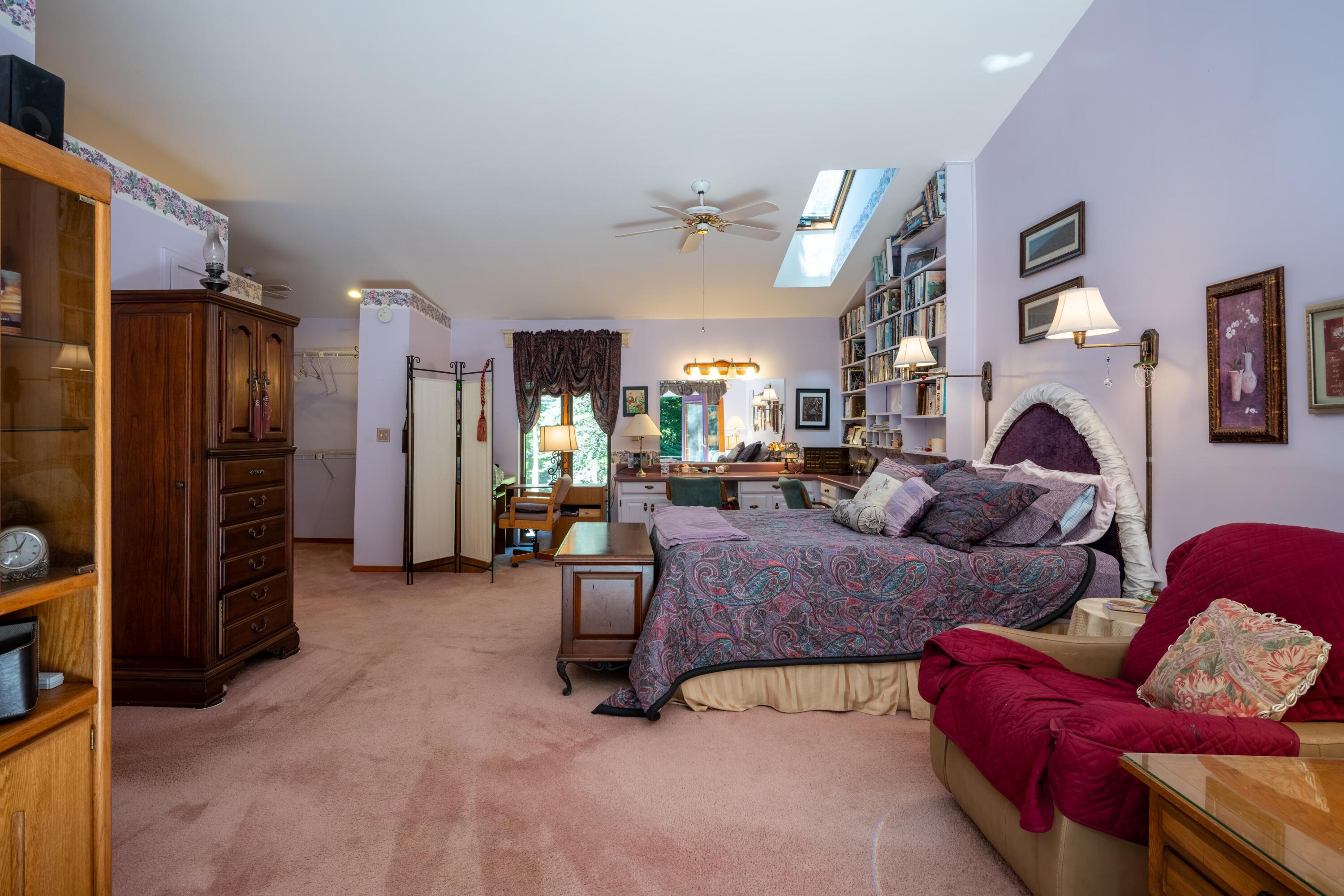 Bedroom with a patterned bed, built-in bookcase, skylight, and red armchair.
