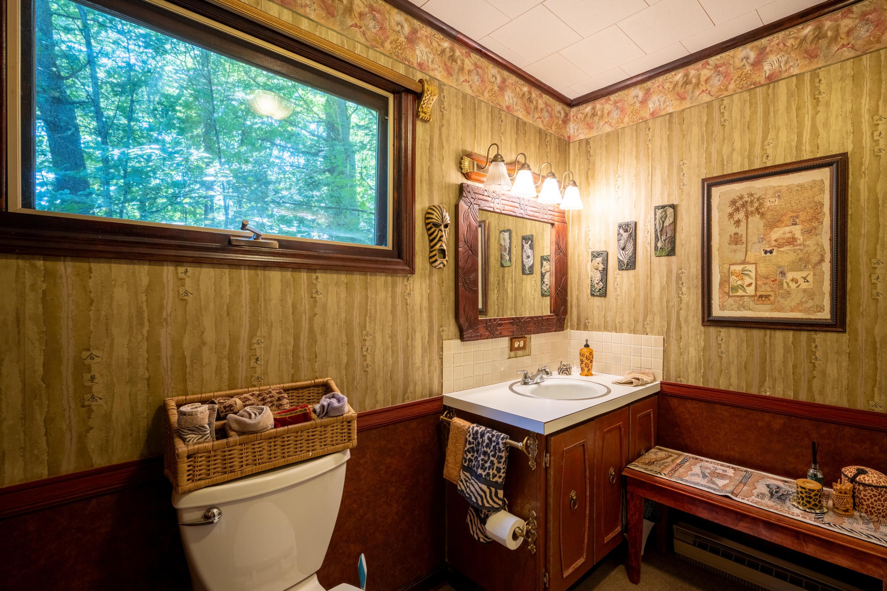 Bathroom with a wood vanity, framed mirror, and wide window overlooking leafy trees.