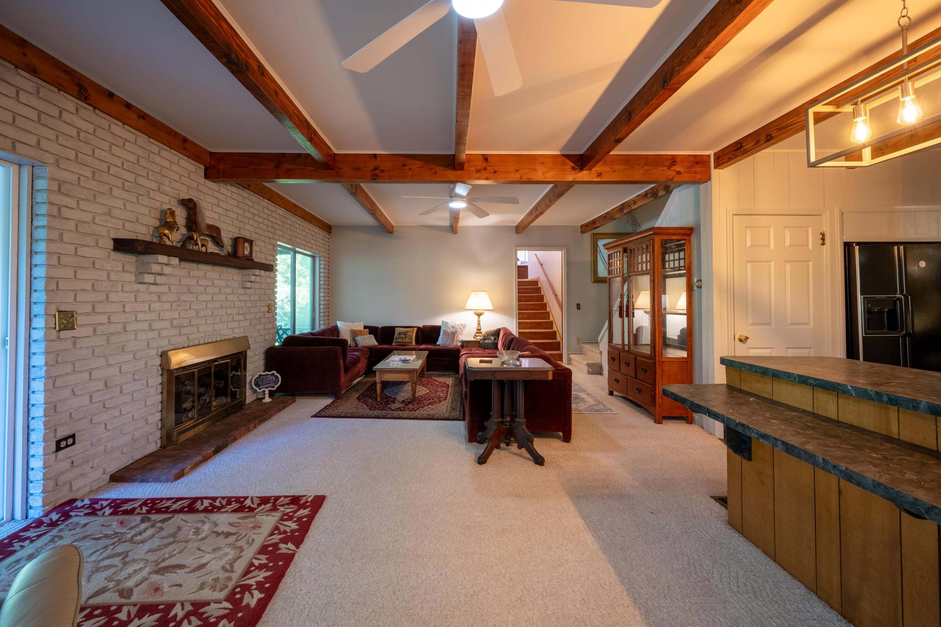 Living room with exposed timber beams, a white brick fireplace, and burgundy sectional seating.