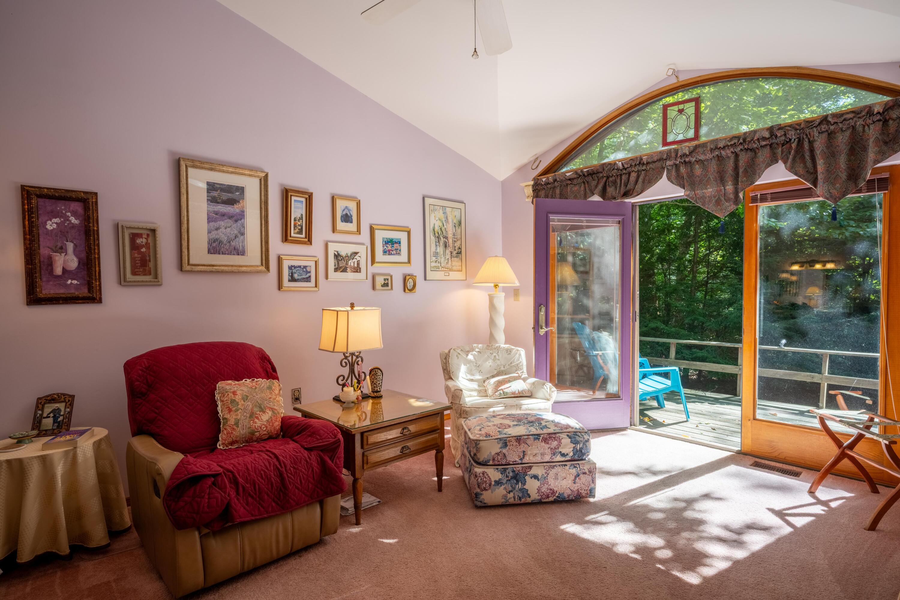 Sitting room with a red recliner and arched windows overlooking a wooded deck.