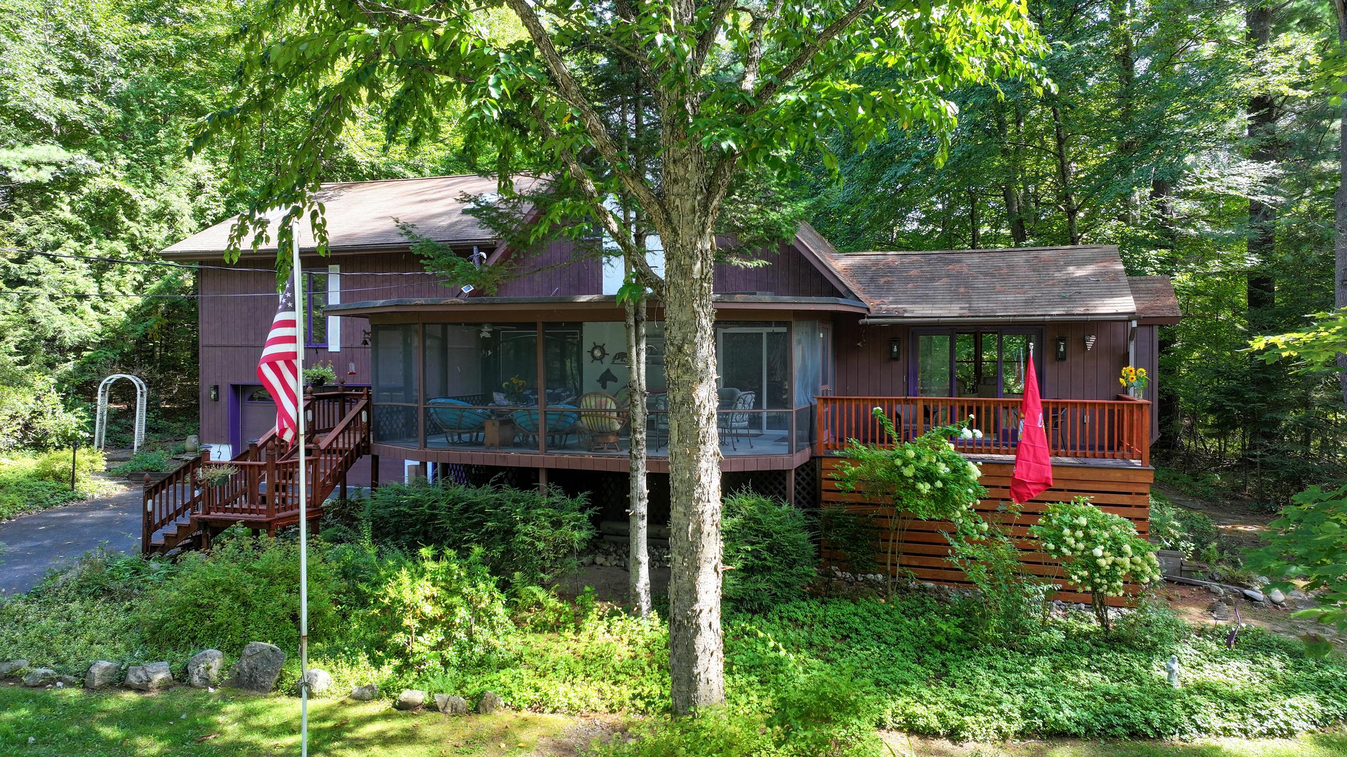 Wood-sided home nestled in the woods, with a large screened porch and decks.