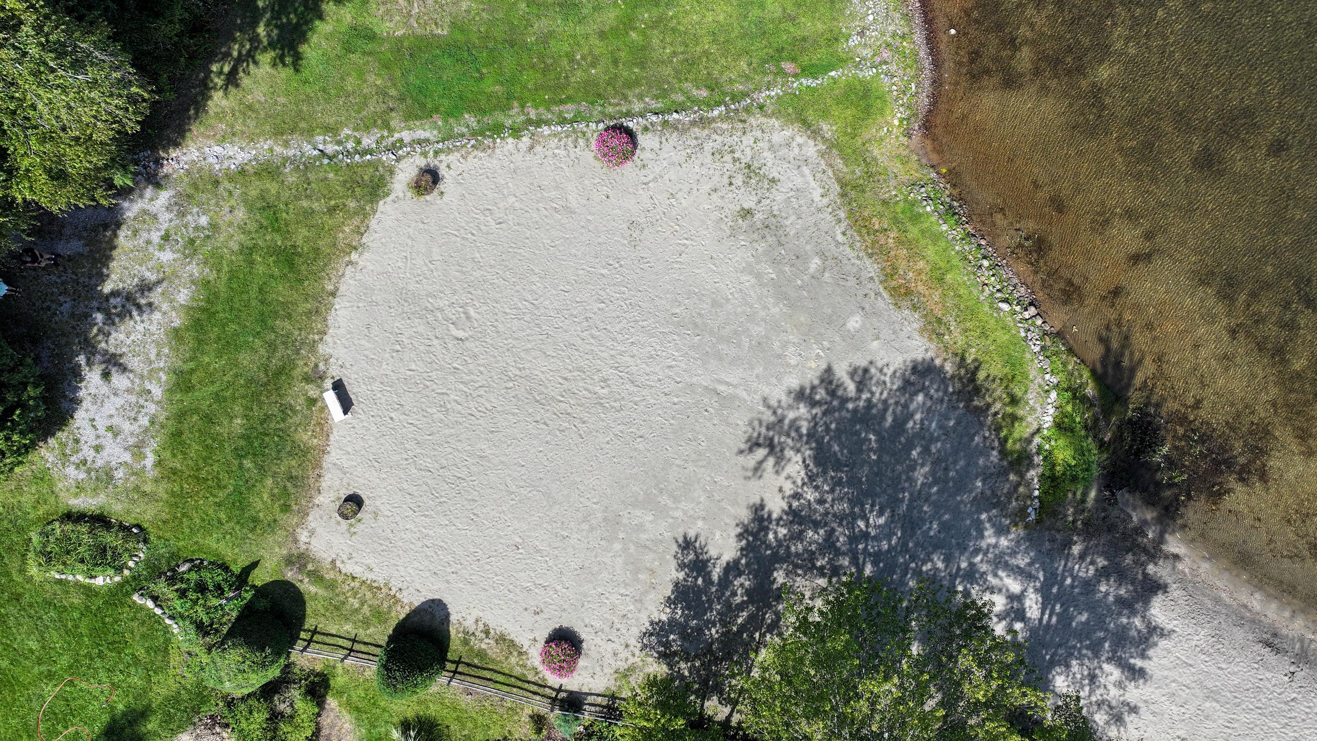 Aerial view of a sandy lakeside beach bordered by lawn and a stone shoreline.