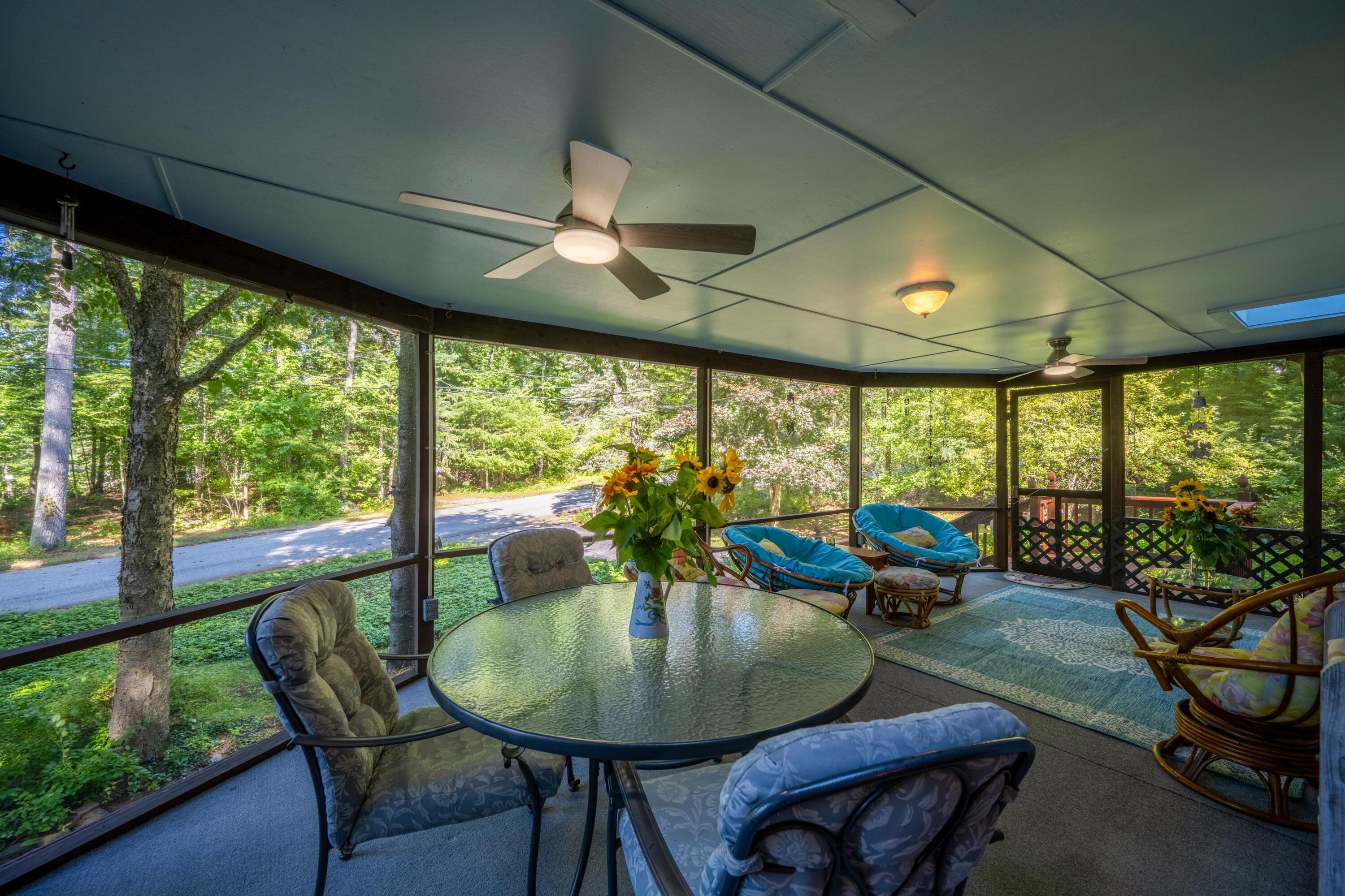 Screened porch with glass table, wicker lounge chairs, ceiling fans, and leafy woodland views.