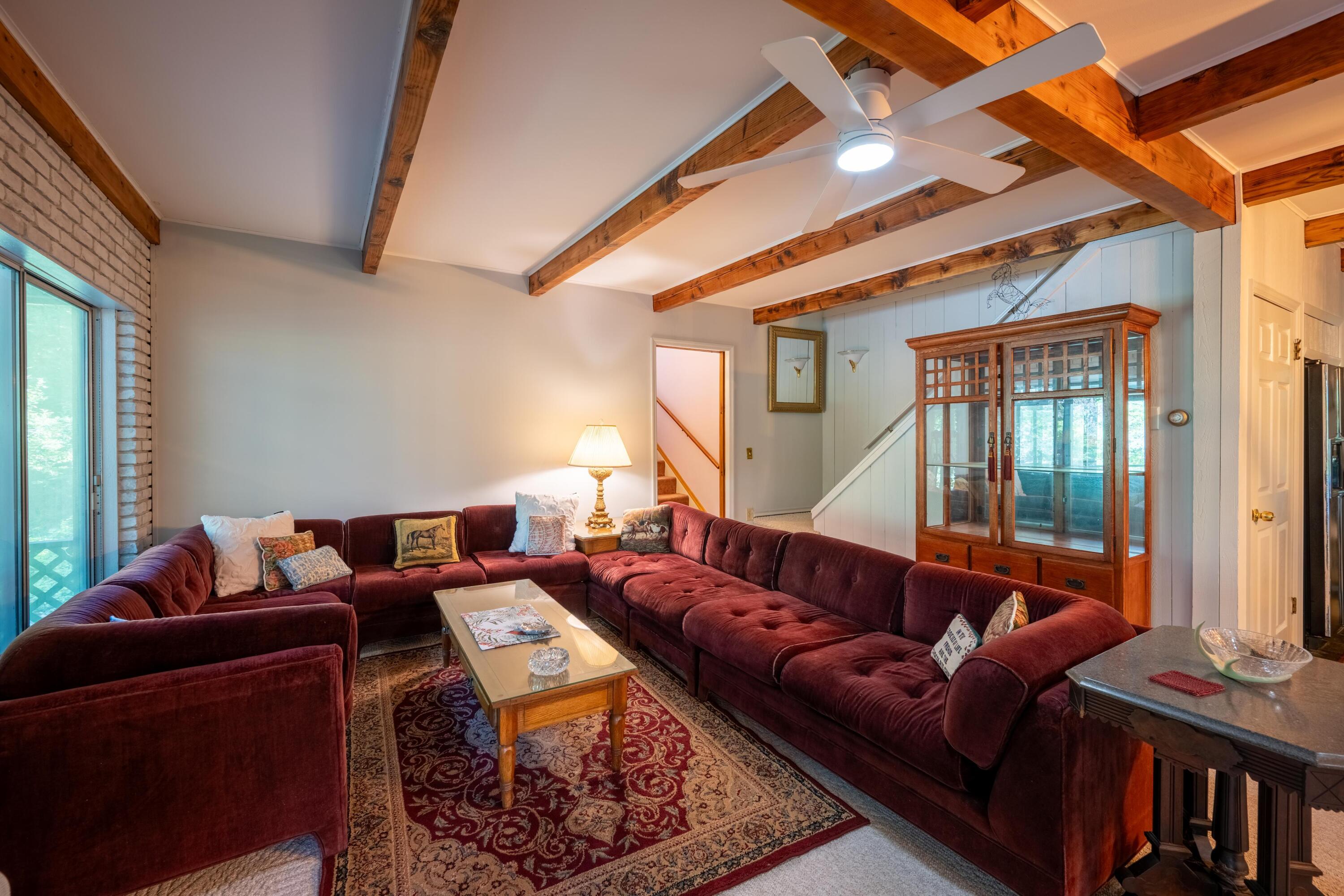 Living room with a burgundy sectional, exposed wooden ceiling beams, and a glass-front cabinet.