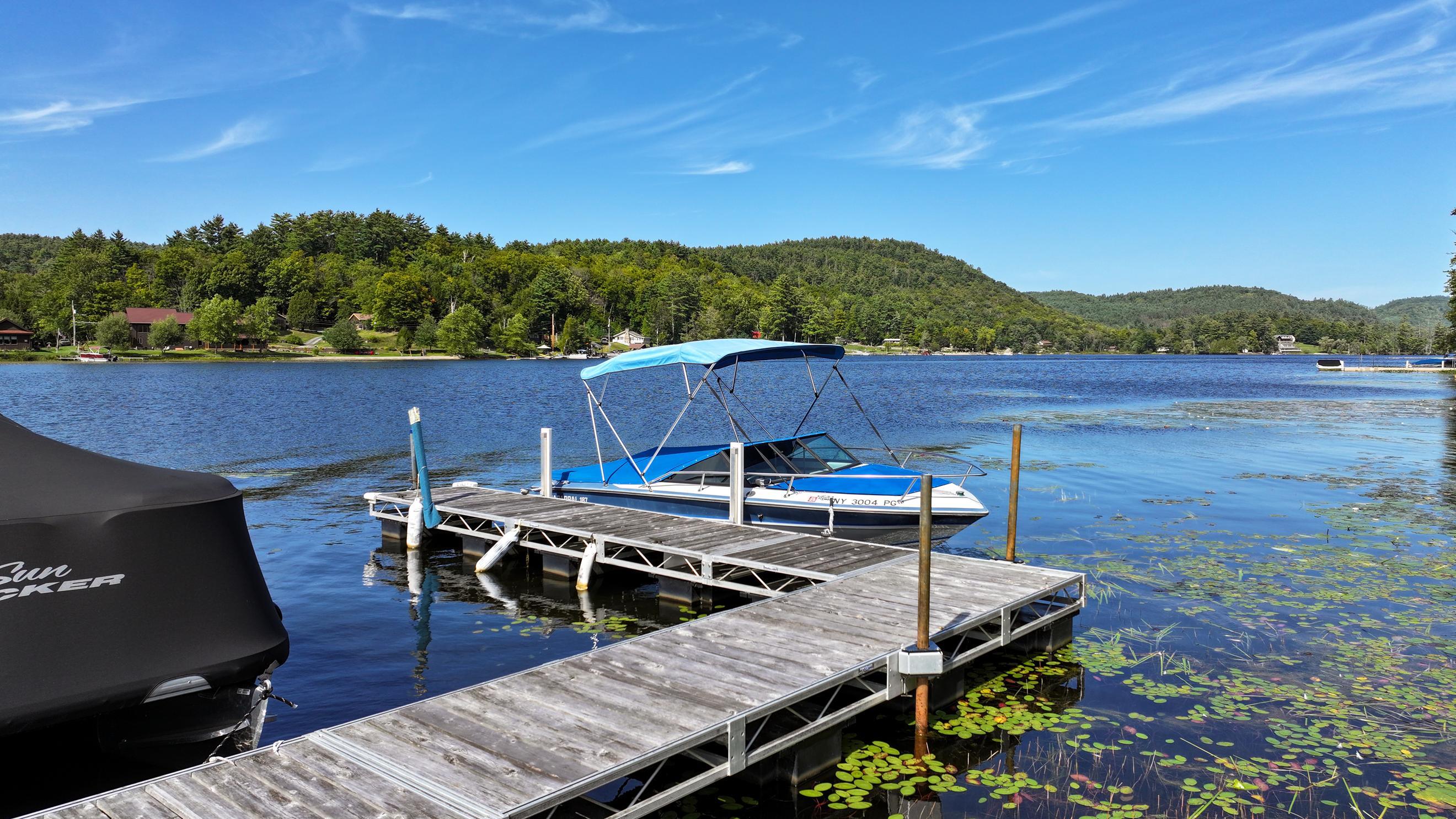 Wooden dock and boats on Brant Lake, with lily pads and wooded hills across the water.