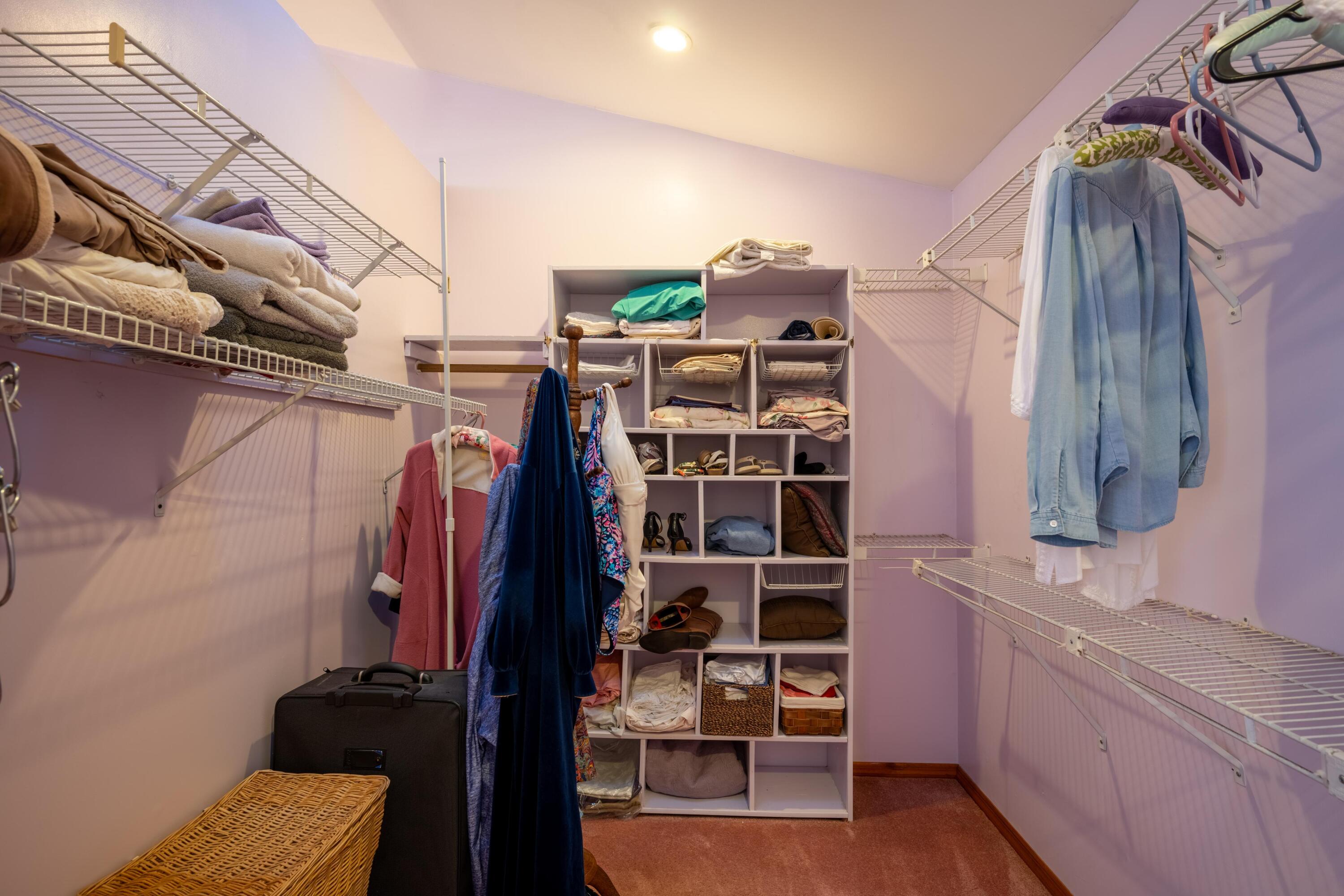 Walk-in closet with wire shelving, clothing, and a central storage cubby unit.