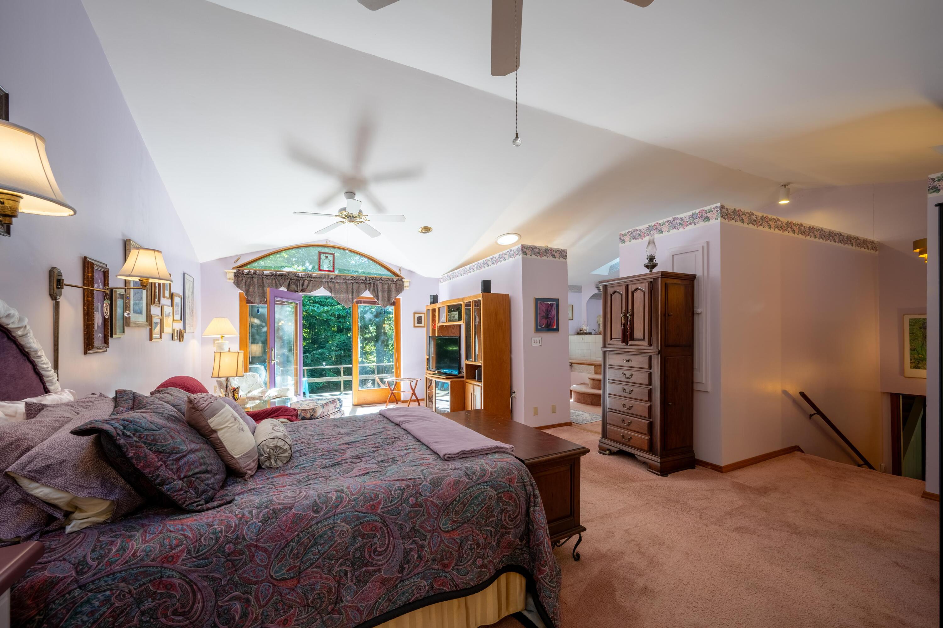 Furnished bedroom with a vaulted ceiling and arched window overlooking trees.