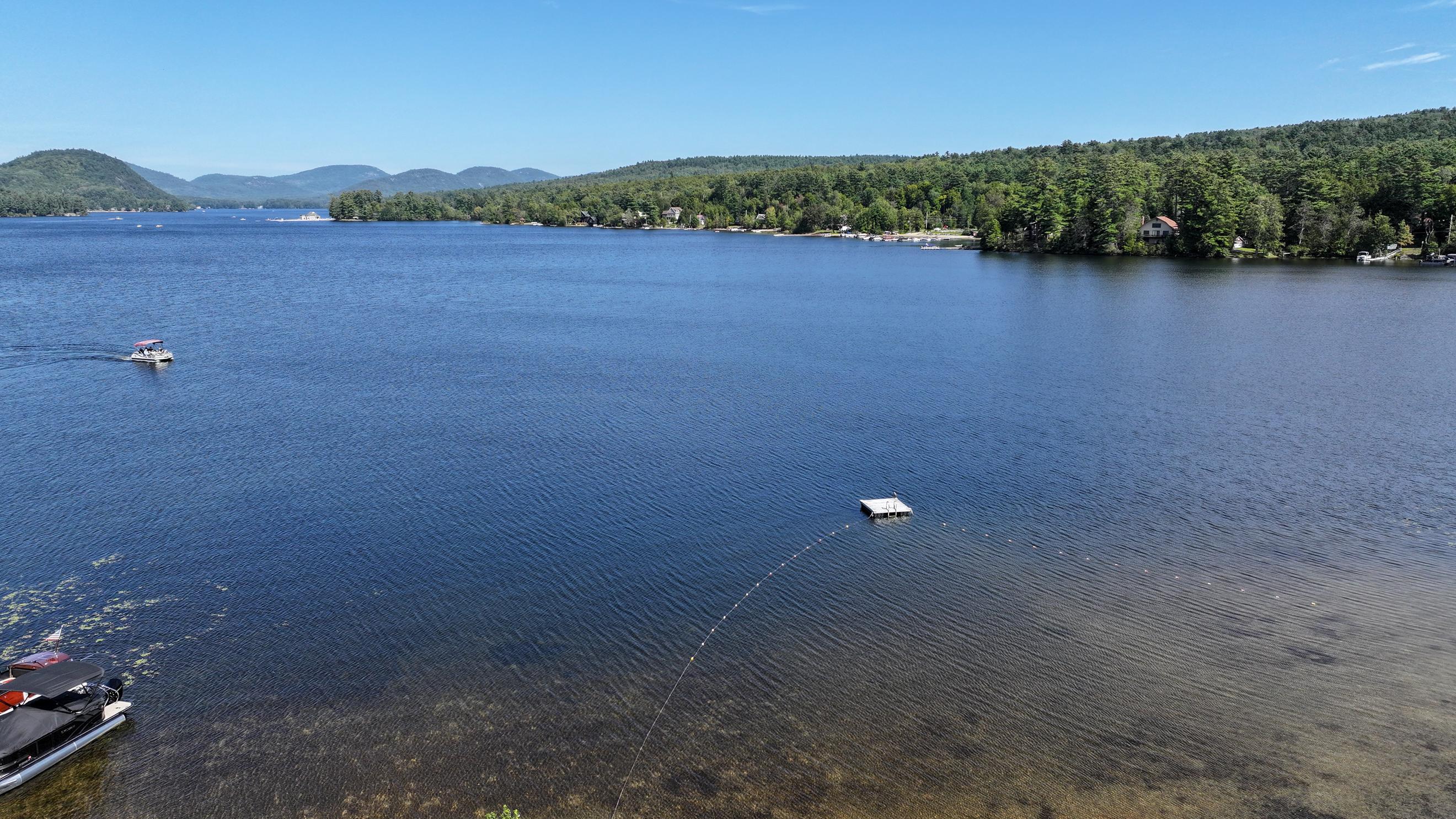 Aerial lake view with forested hills, a boat, and a floating dock.