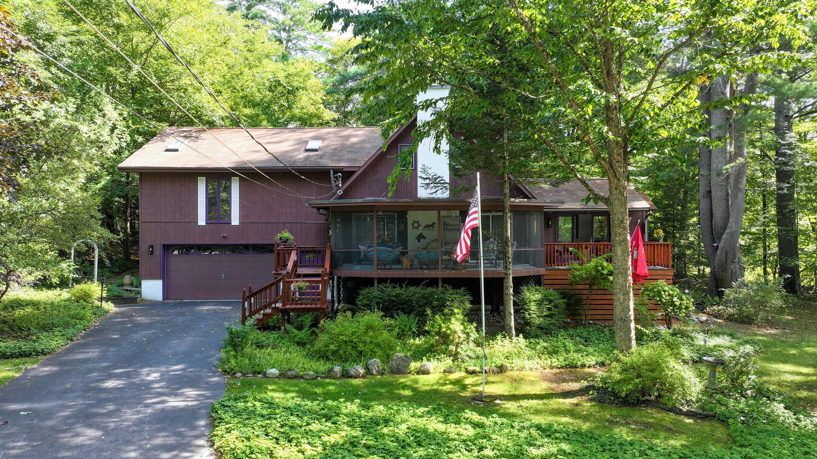 Wood-sided house with a screened porch and decks nestled among mature trees.