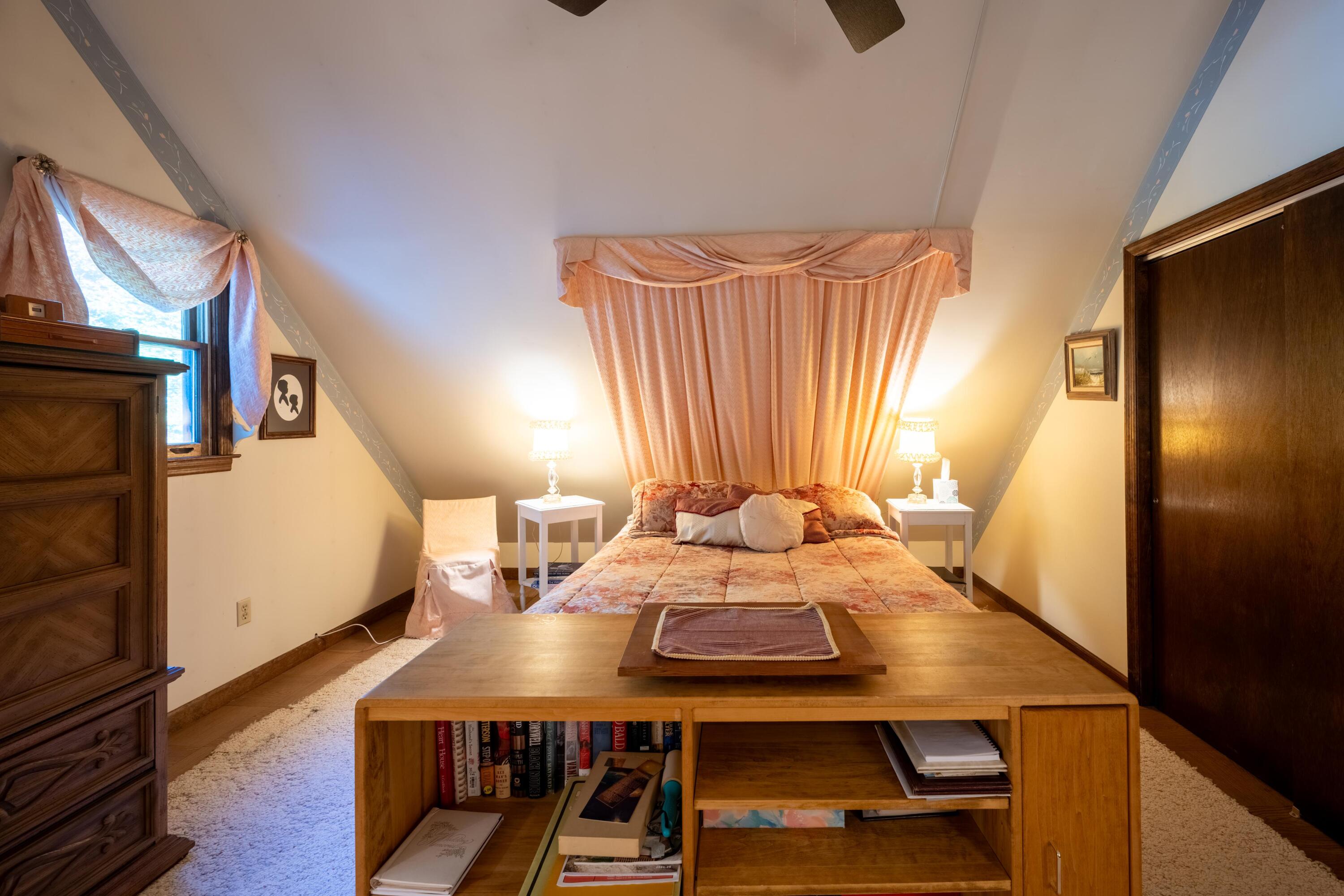 Attic bedroom with a double bed, peach curtains, sloped ceiling, and wooden desk.