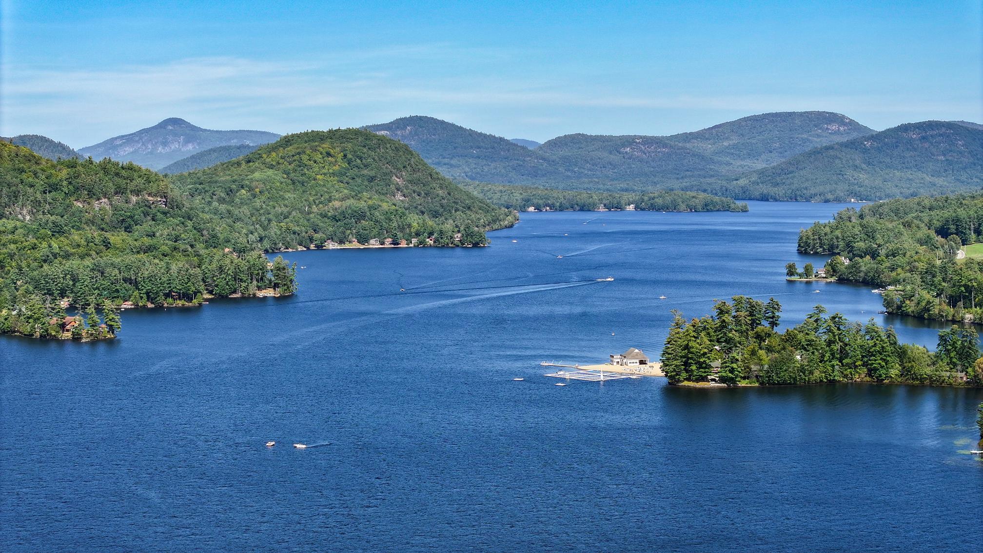 Blue lake with boats, wooded shorelines, and forested mountains beyond.