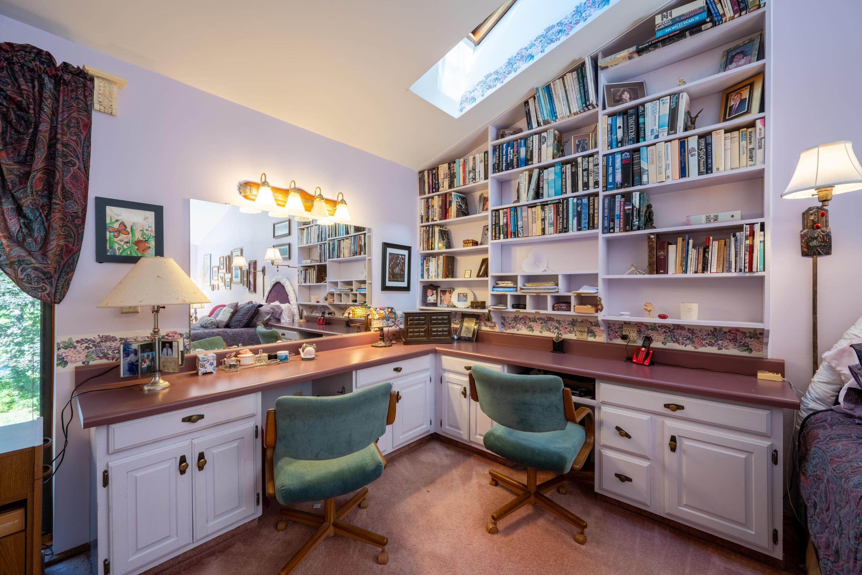 Home office with built-in bookshelves, wraparound desk, two green chairs, and a skylight.