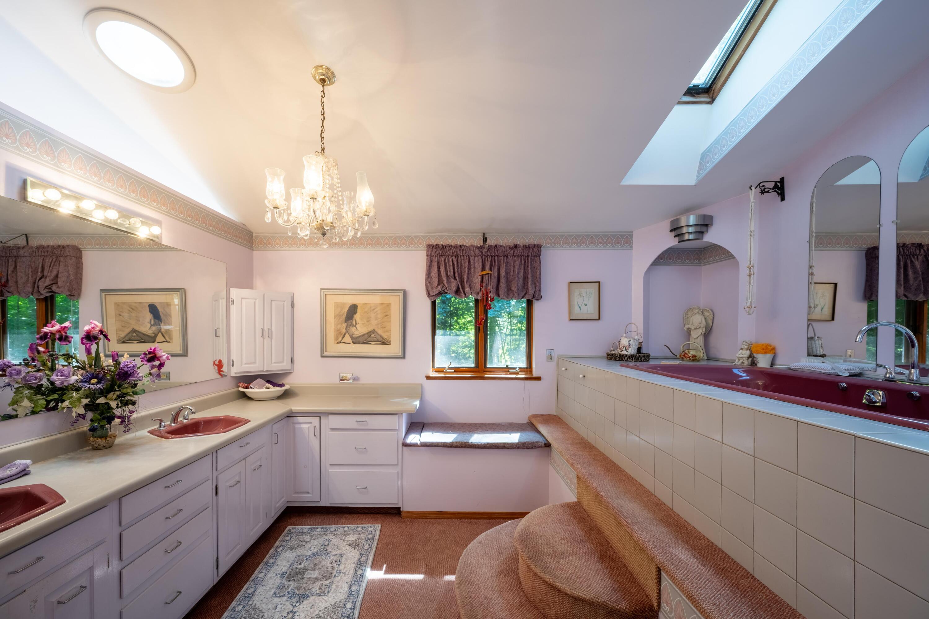 Spacious bathroom with a burgundy jetted tub, dual vanity, and skylight.