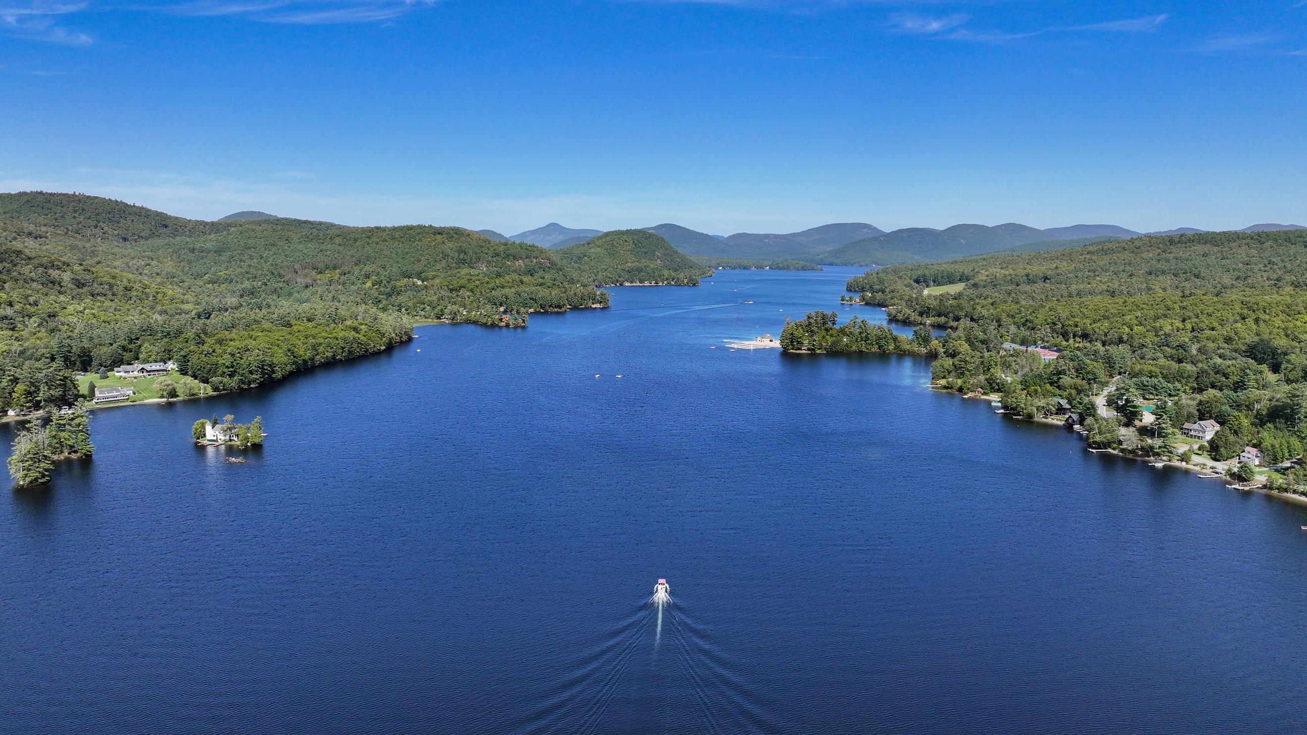 Aerial view of a mountain lake, with wooded shores, waterfront homes, and a boat wake.