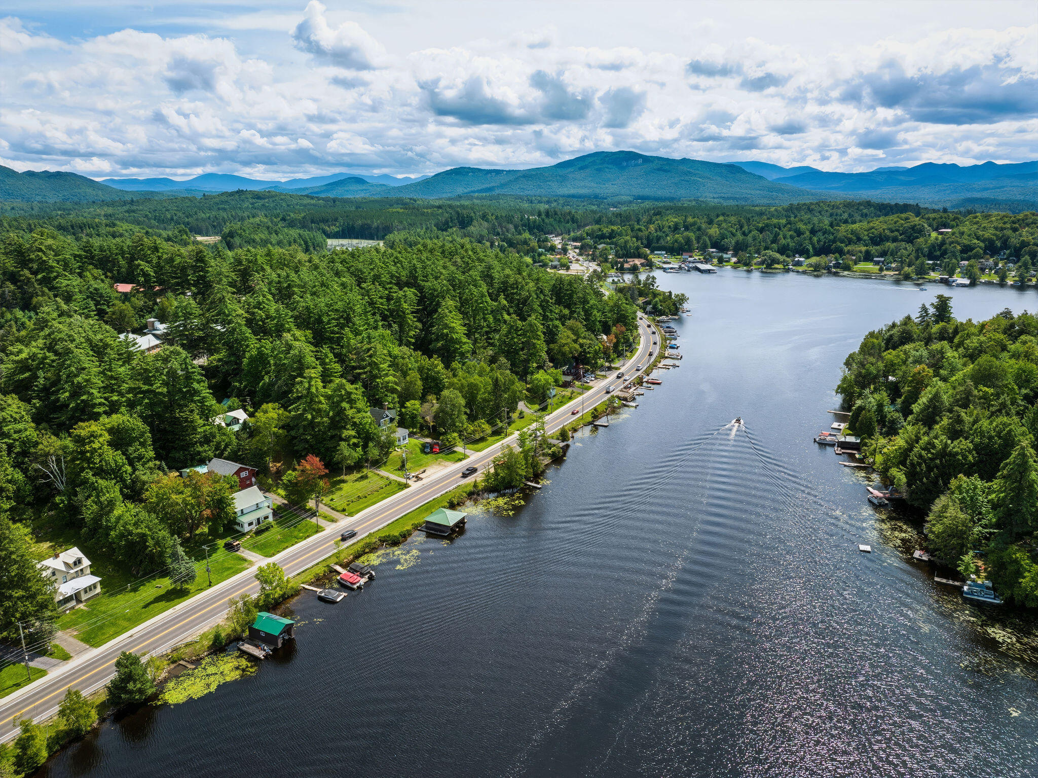 Aerial view of Lake Flower, with a shoreline road, wooded homes, and mountains beyond.