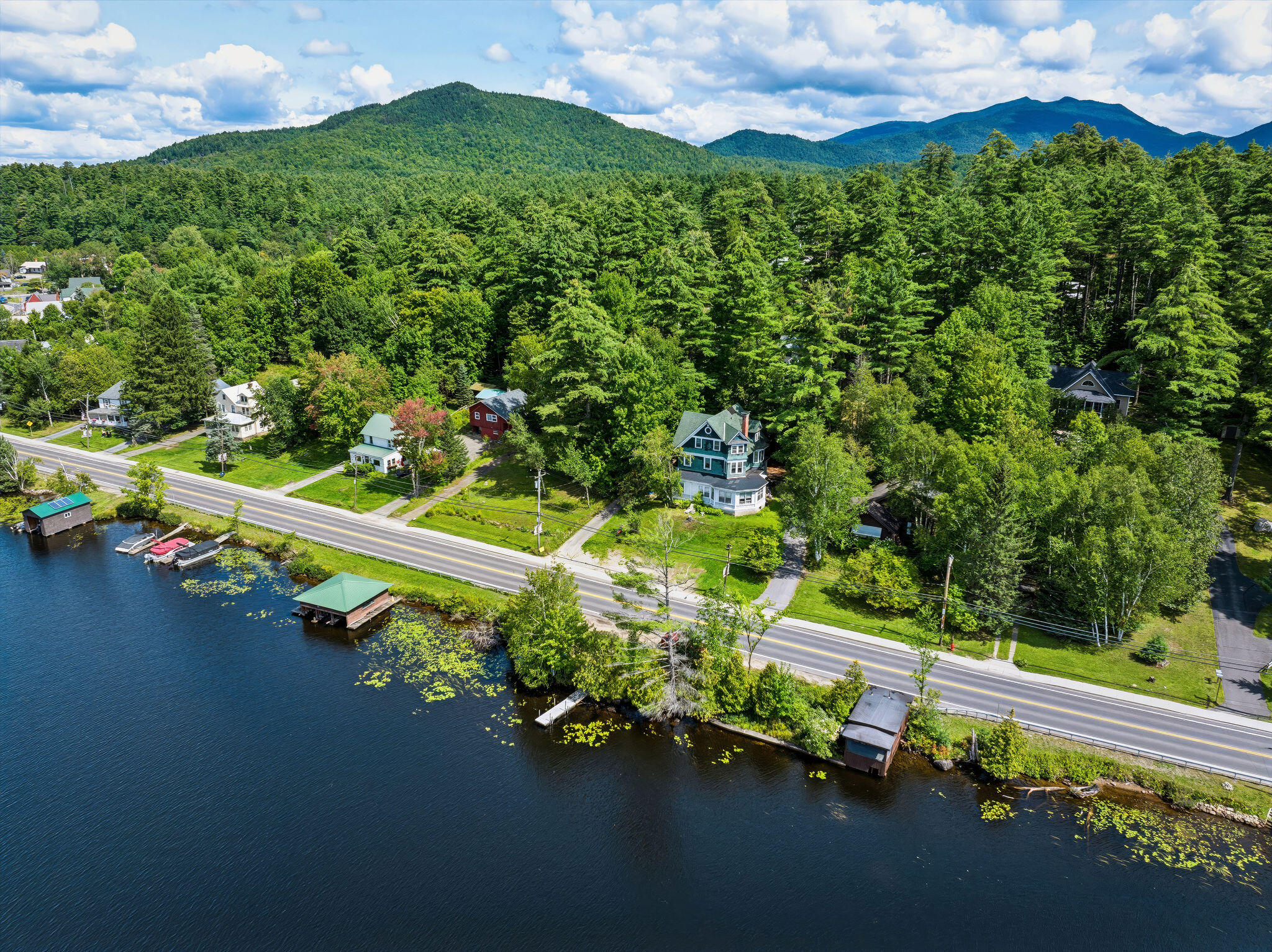Blue-green multi-story house beside the water, with forested mountains in the distance.